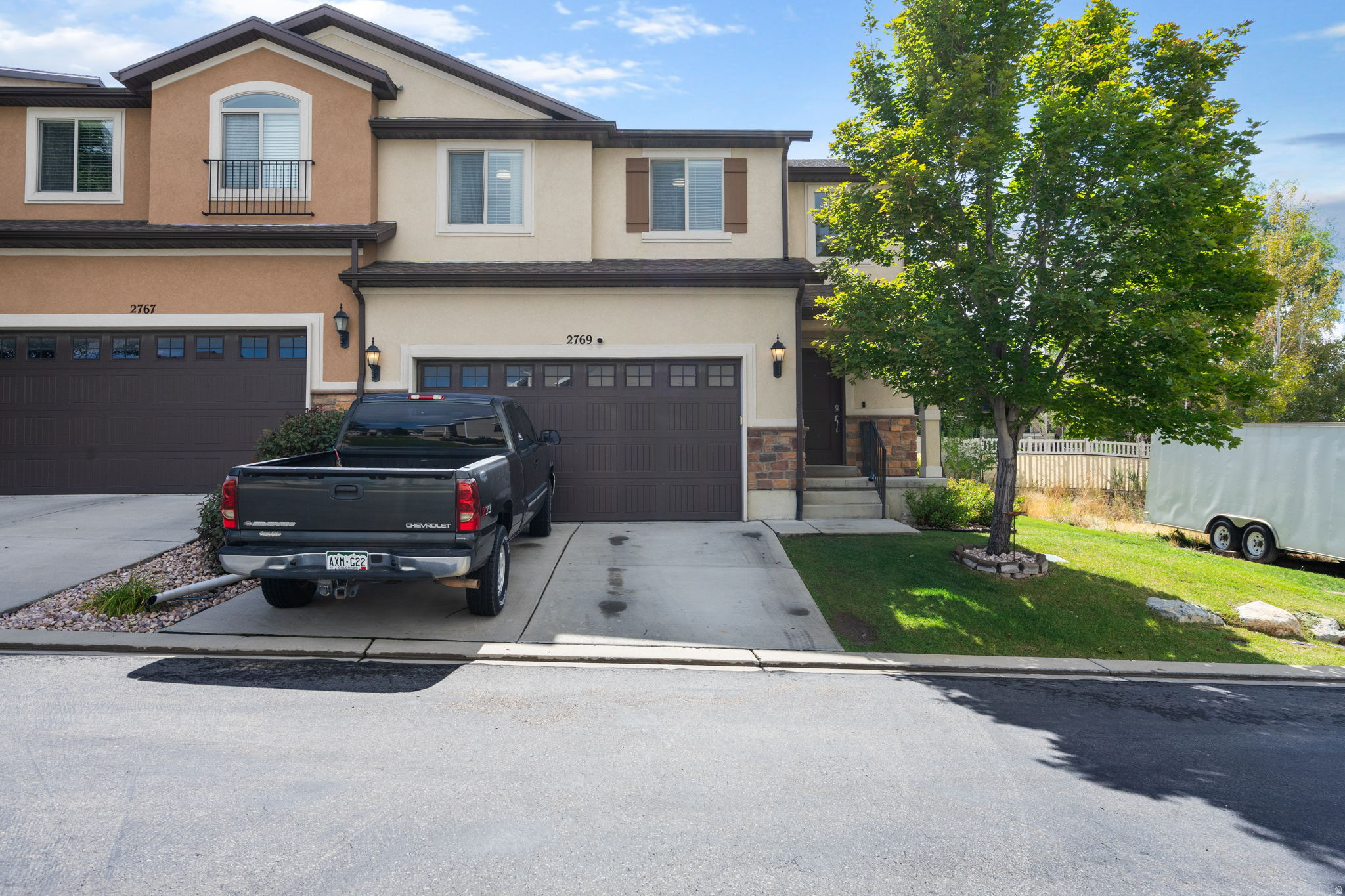 Two-story attached home with a dark garage door, pickup in the driveway, and a large leafy tree.