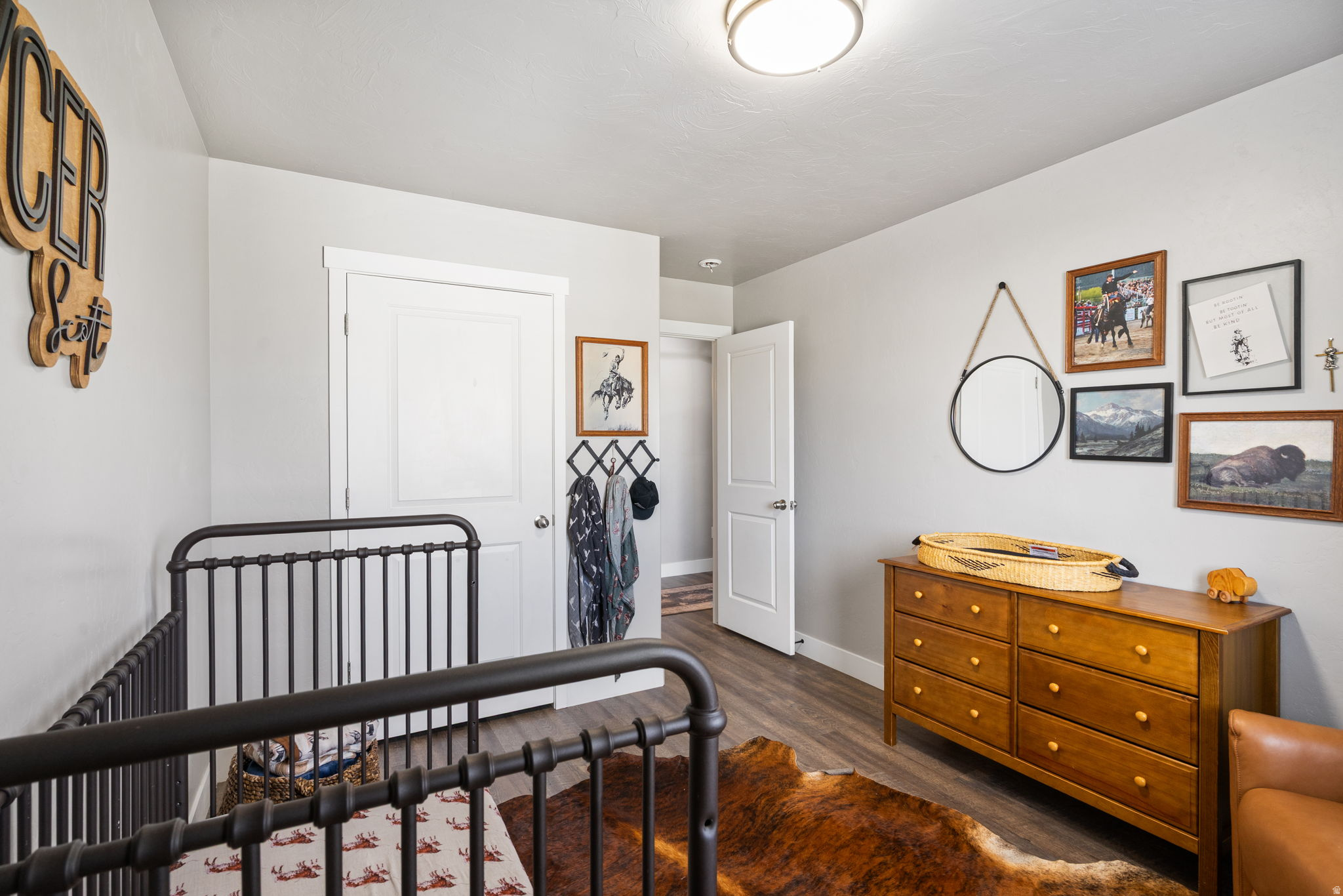 Bedroom with a black metal bed, wooden dresser, cowhide rug, and western-themed wall art.