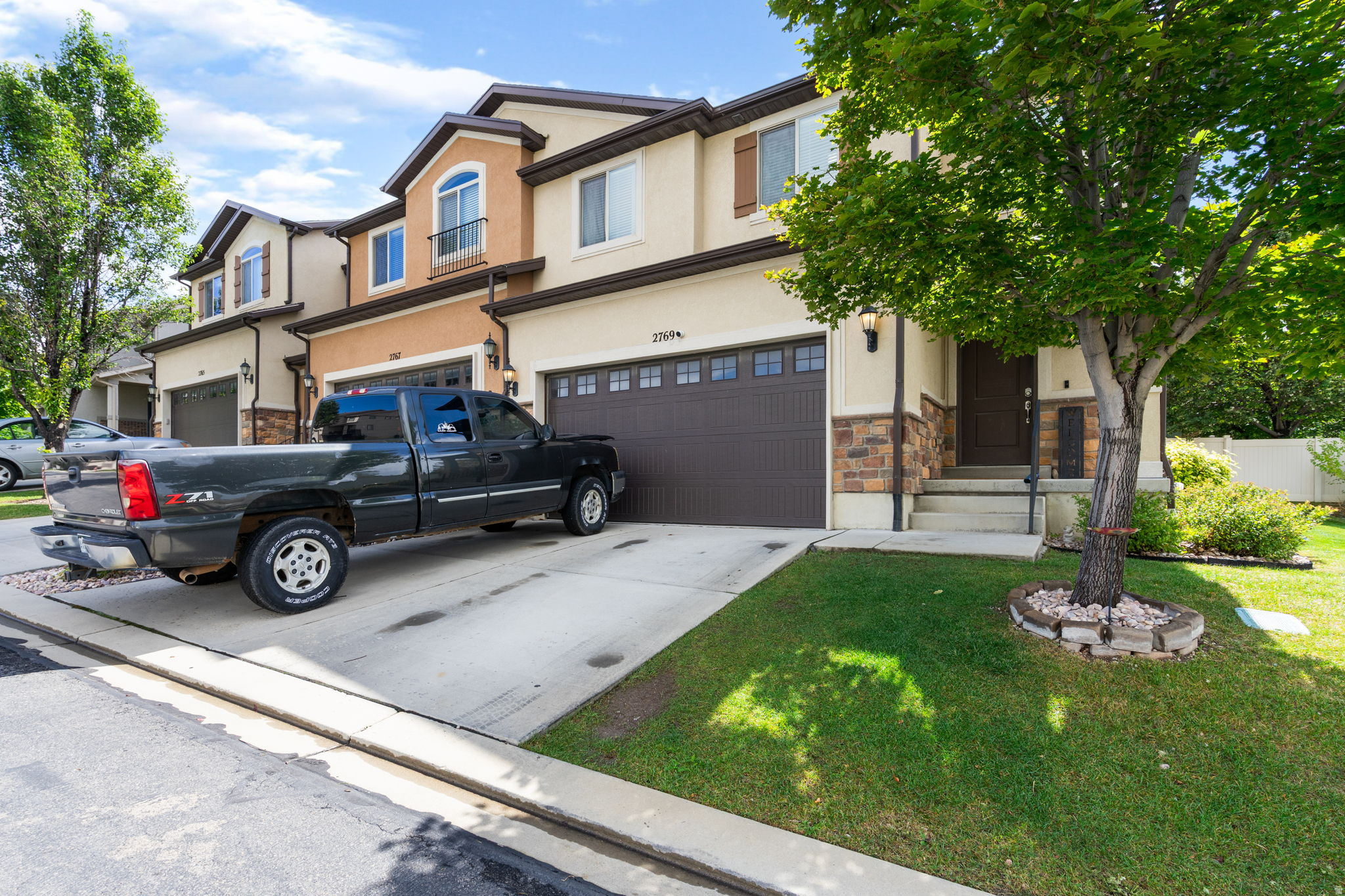 Attached home with tan stucco, dark double garage door, and a pickup truck in the driveway.