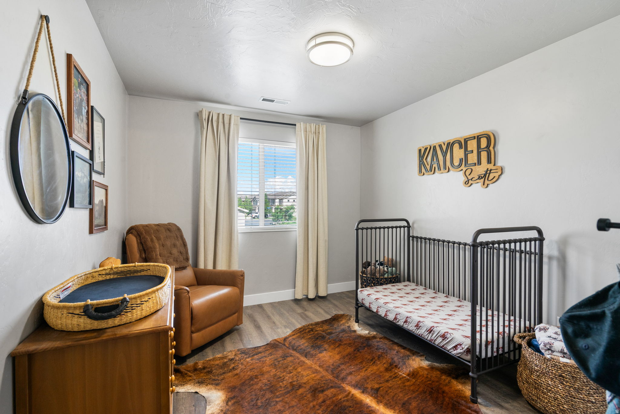 Nursery bedroom with a black metal crib, brown leather armchair, and cowhide-style rug.