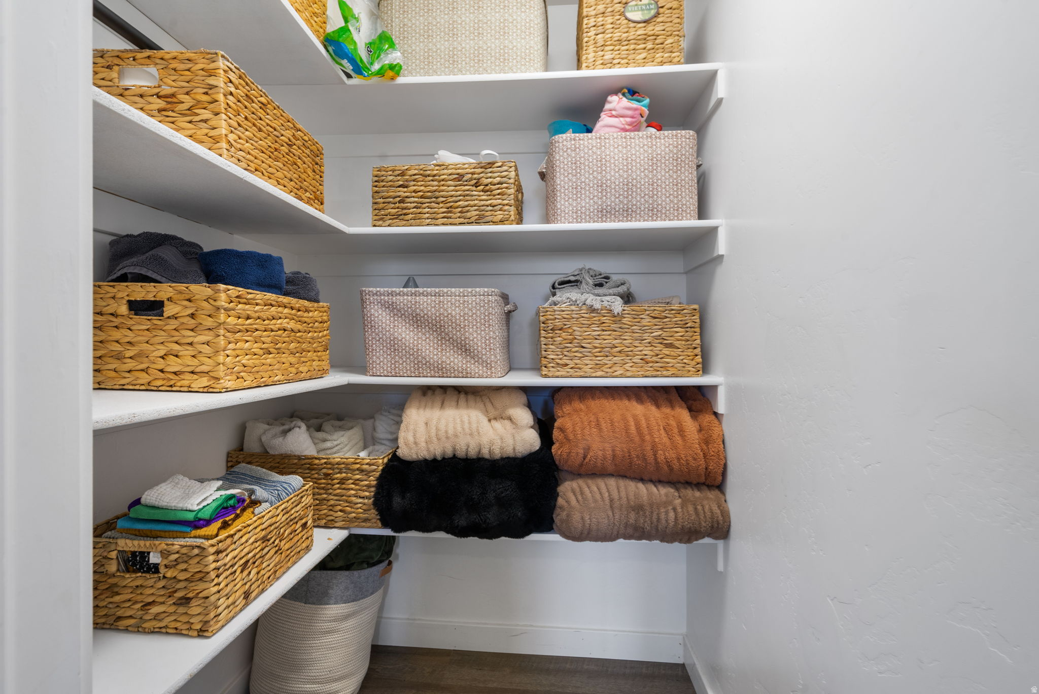 Walk-in linen closet with woven baskets and neatly folded towels and blankets on white shelves.