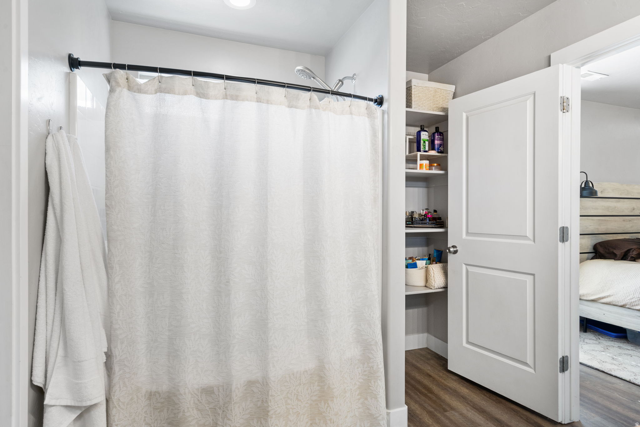 Bathroom with a patterned shower curtain and open storage closet beside the doorway to a bedroom.