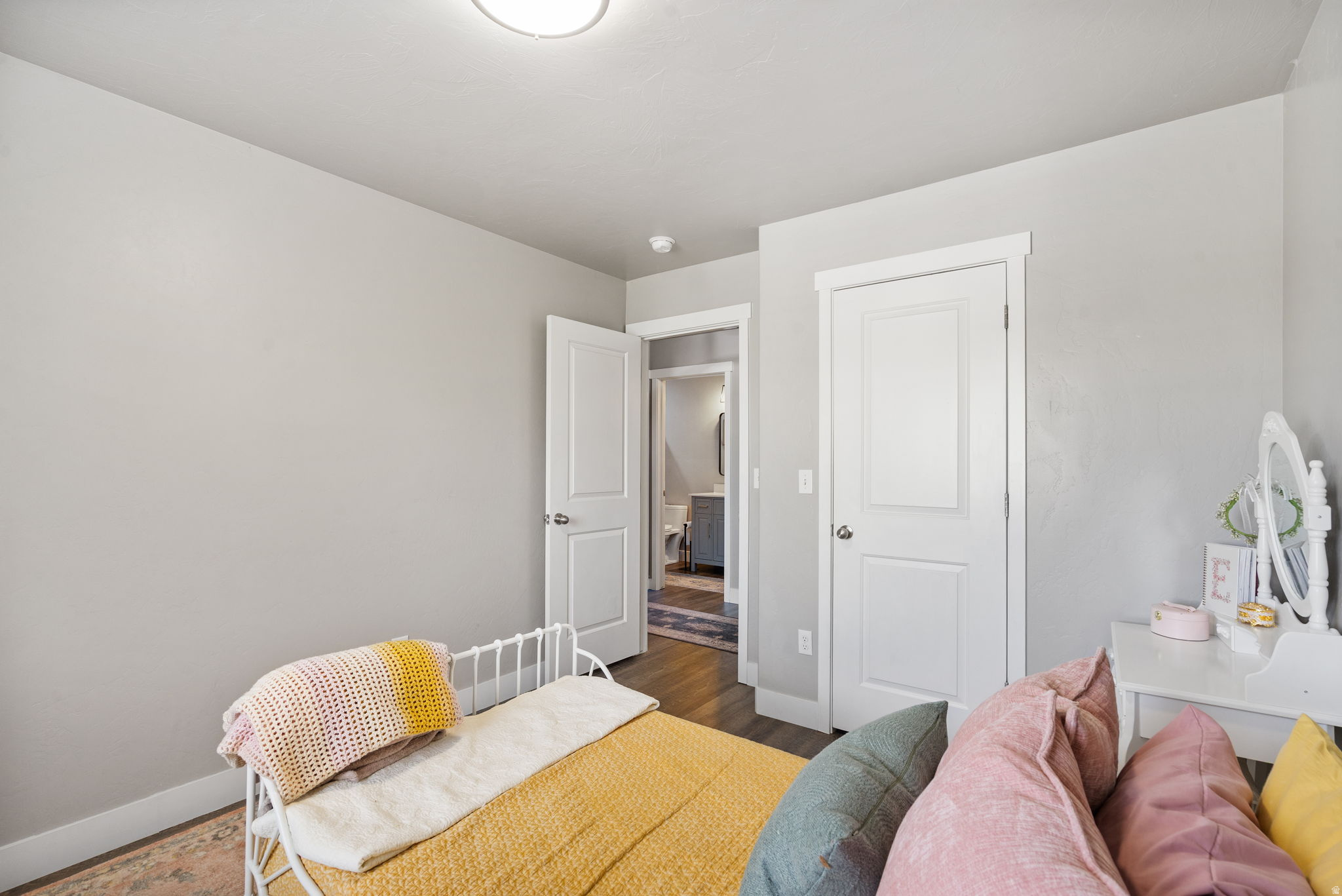 Bedroom with a white daybed, mustard bedding, colorful pillows, and a vanity.