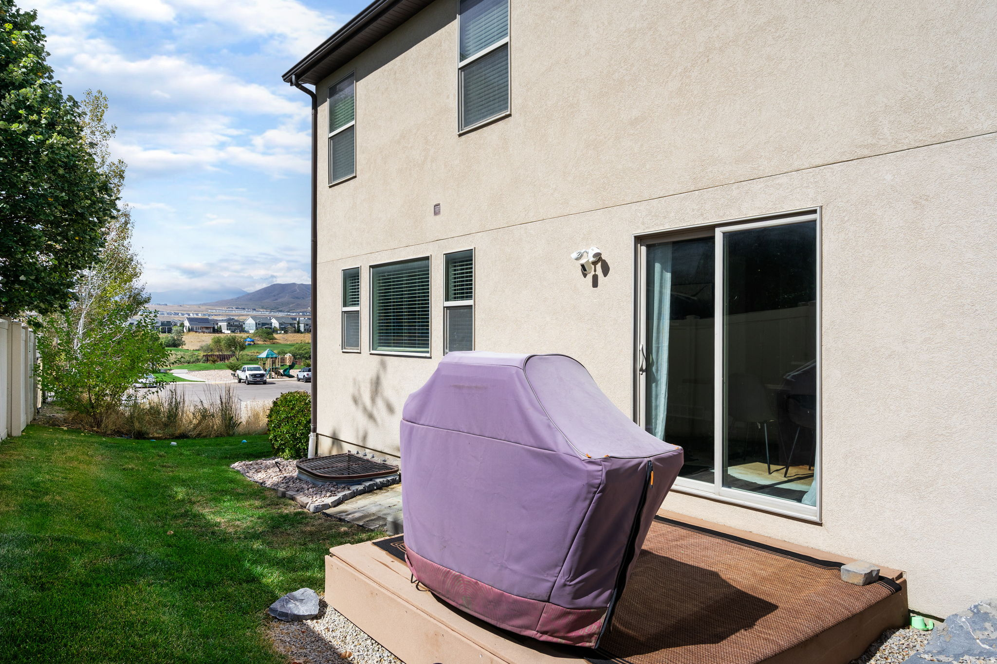 Home’s rear patio with a covered grill, green lawn, and distant mountain view.
