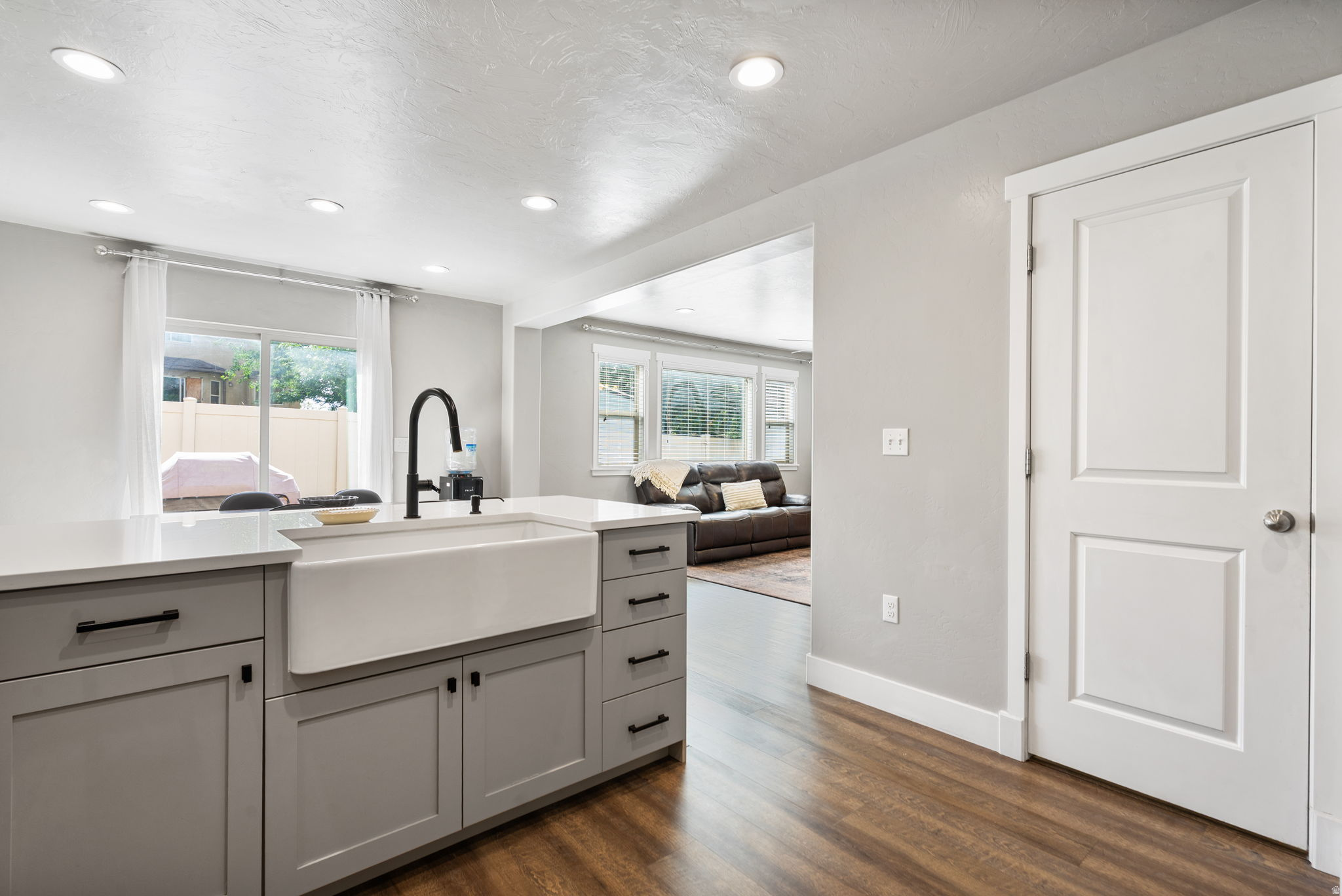 Kitchen with a white farmhouse sink opening to a living area with a leather sofa.