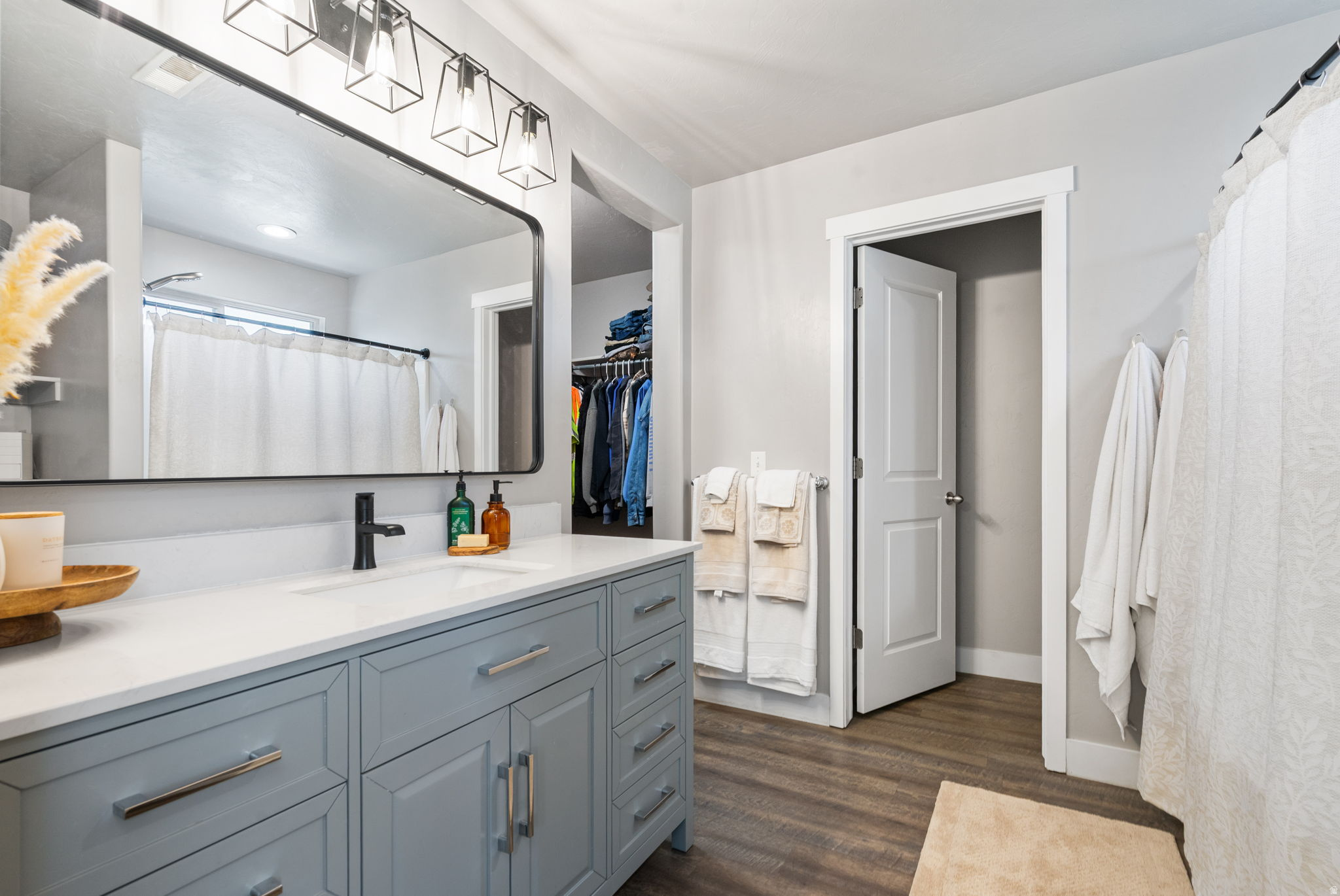 Bathroom with a gray-blue vanity, large mirror, and open closet with hanging clothes.