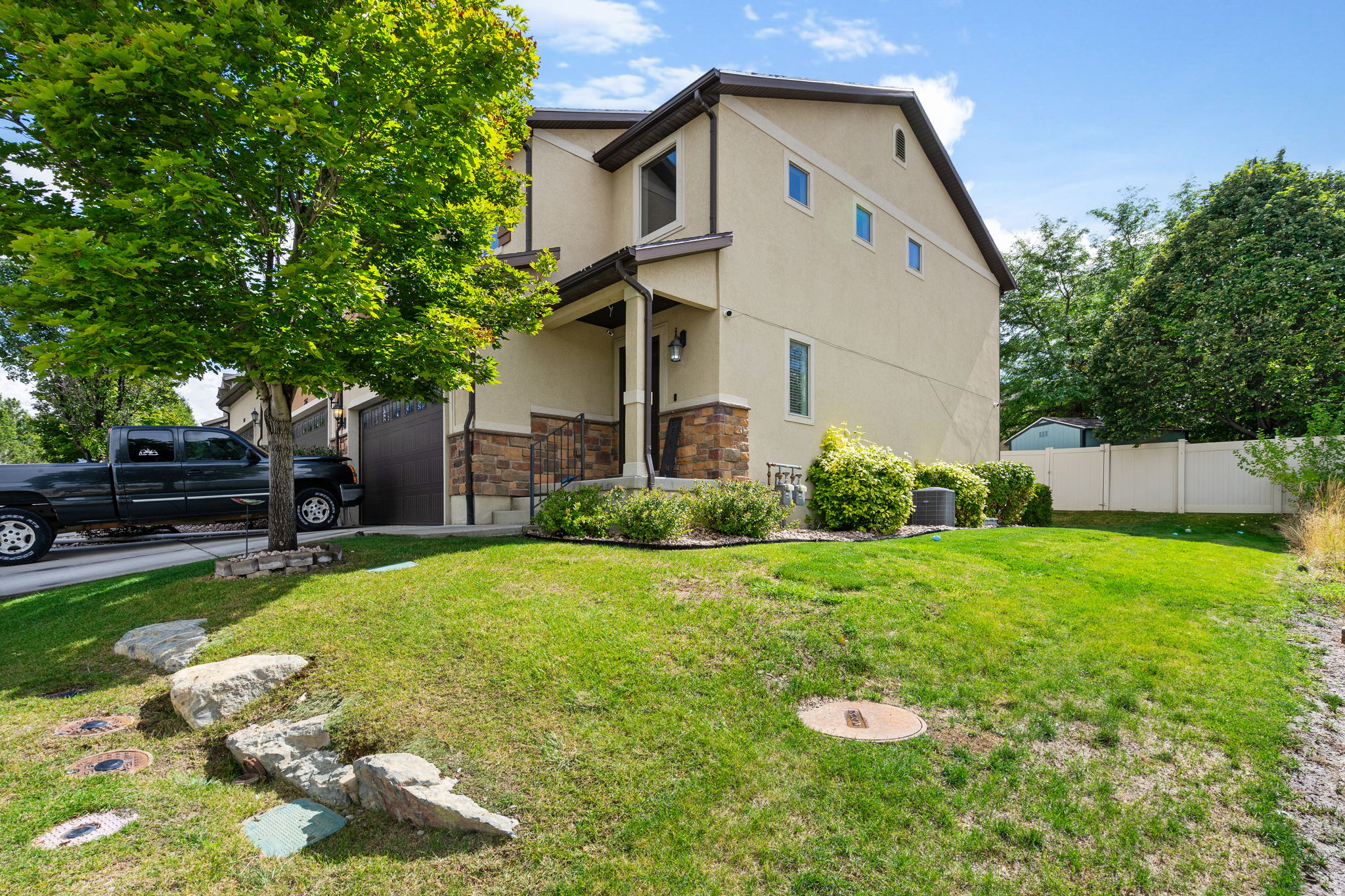 Two-story beige stucco home with stone accents, an attached garage, and a fenced green lawn.