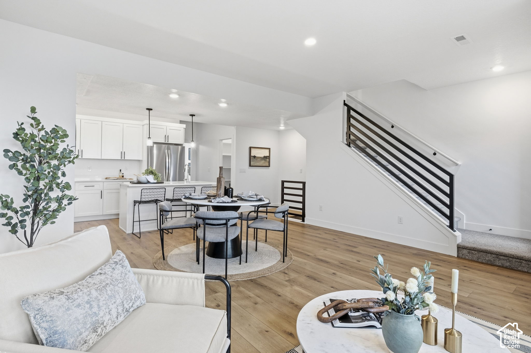 Open-plan kitchen and dining area with white cabinetry, a set table, wood floors, and a black-railed staircase.