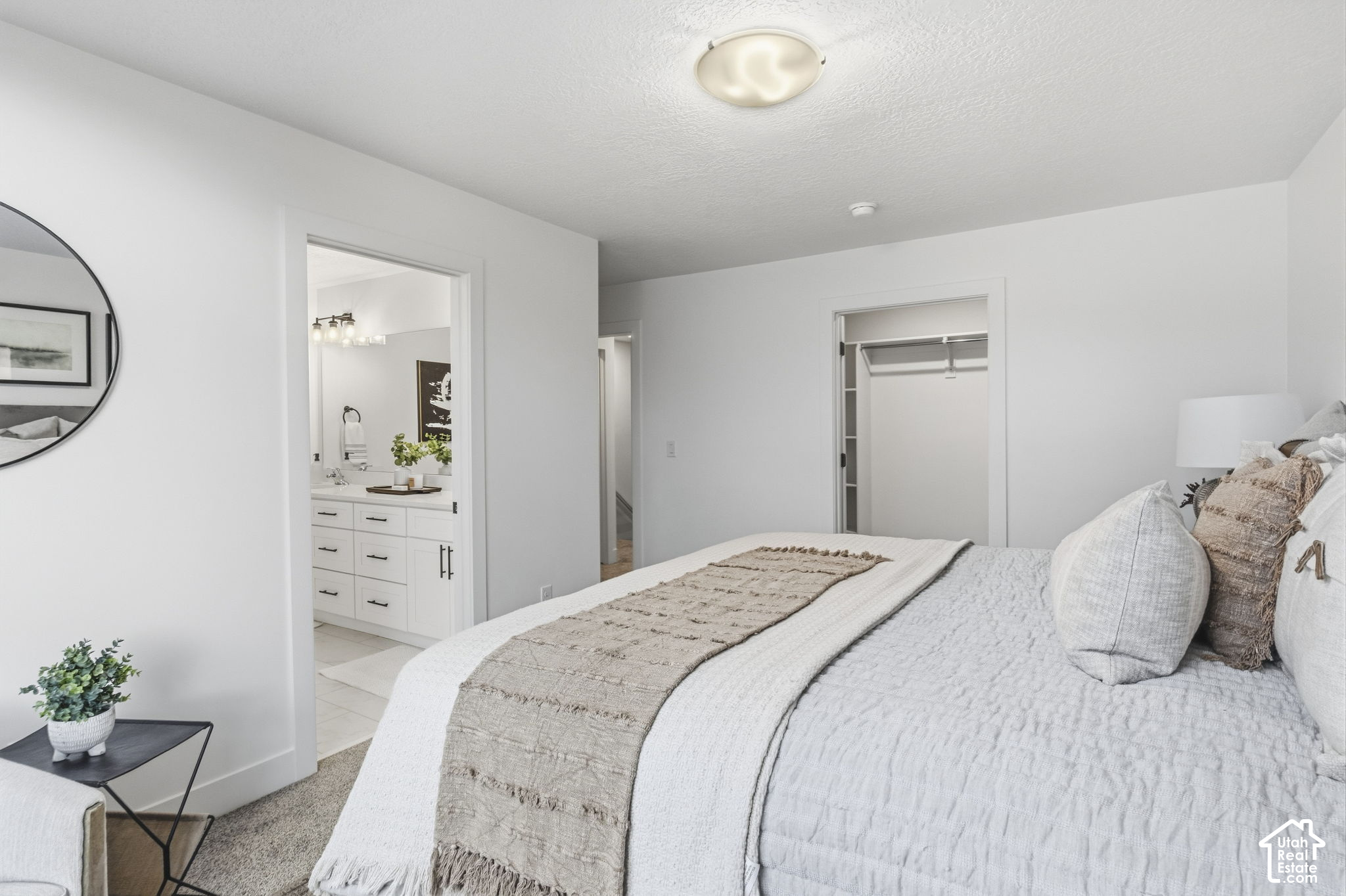 Furnished bedroom with a white bed, beige throw, bathroom vanity doorway, and open closet.
