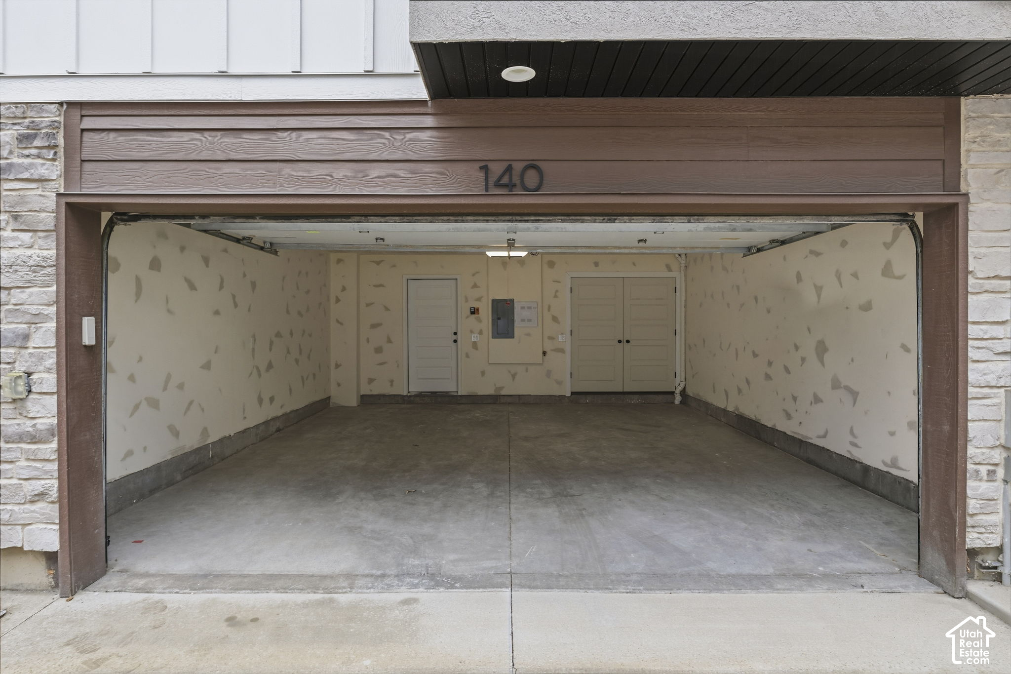 Open empty garage with a concrete floor, patched walls, and double doors at the back.