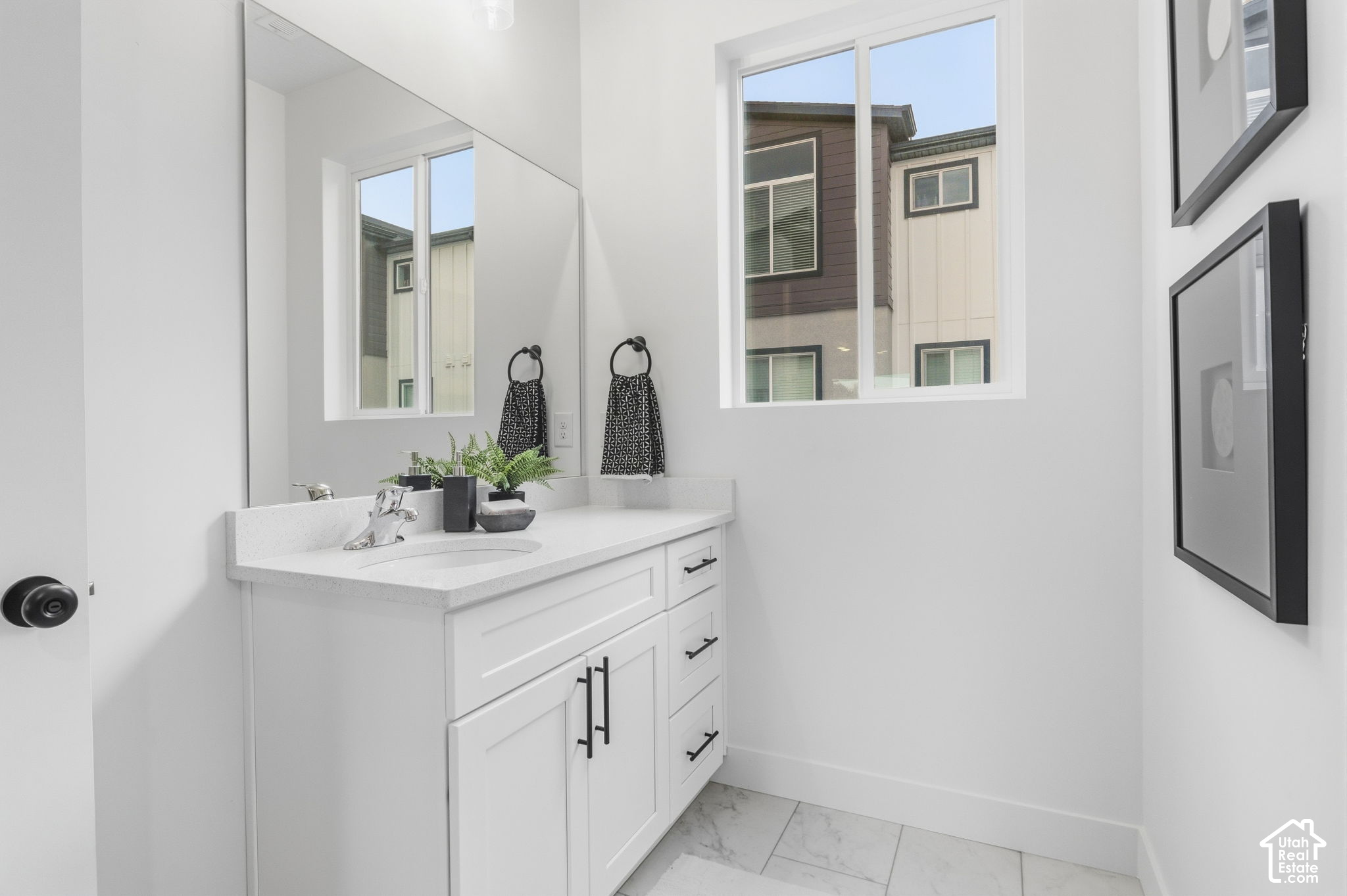 Bathroom vanity with a white countertop, large mirror, and window overlooking a neighboring building.