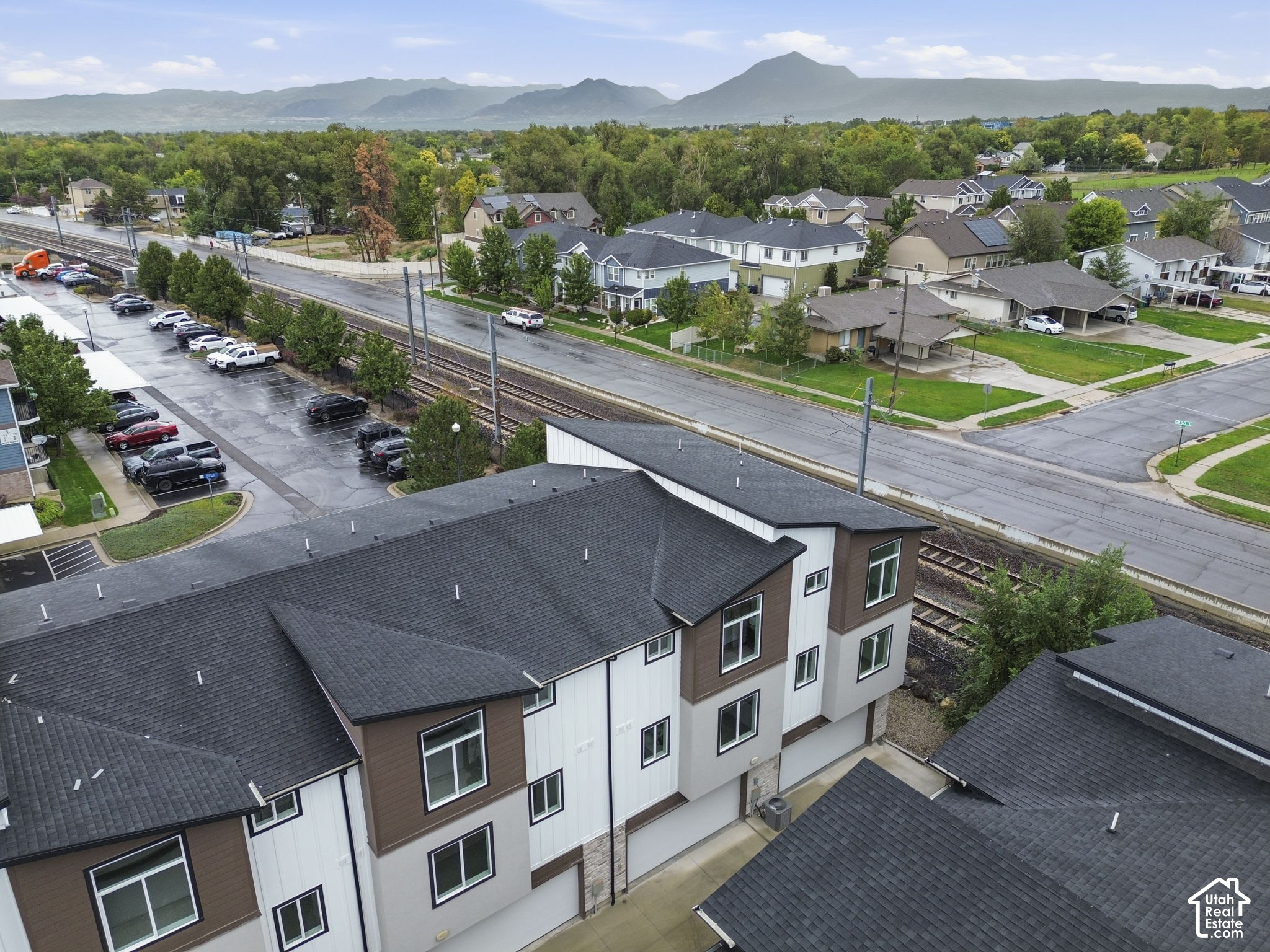 Aerial view of modern townhomes beside railroad tracks, with mountains in the distance.