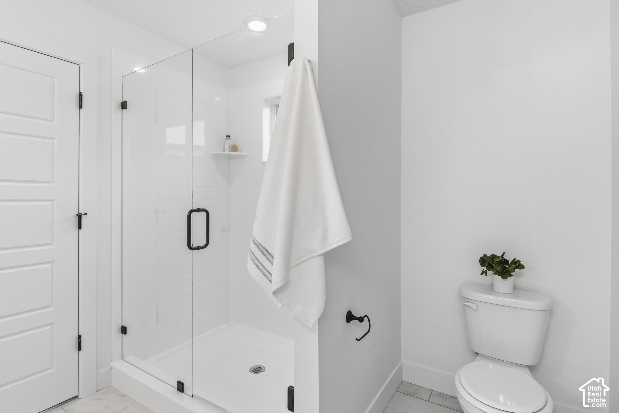 Bright white bathroom with a glass walk-in shower, black hardware, and a towel hanging beside the toilet.