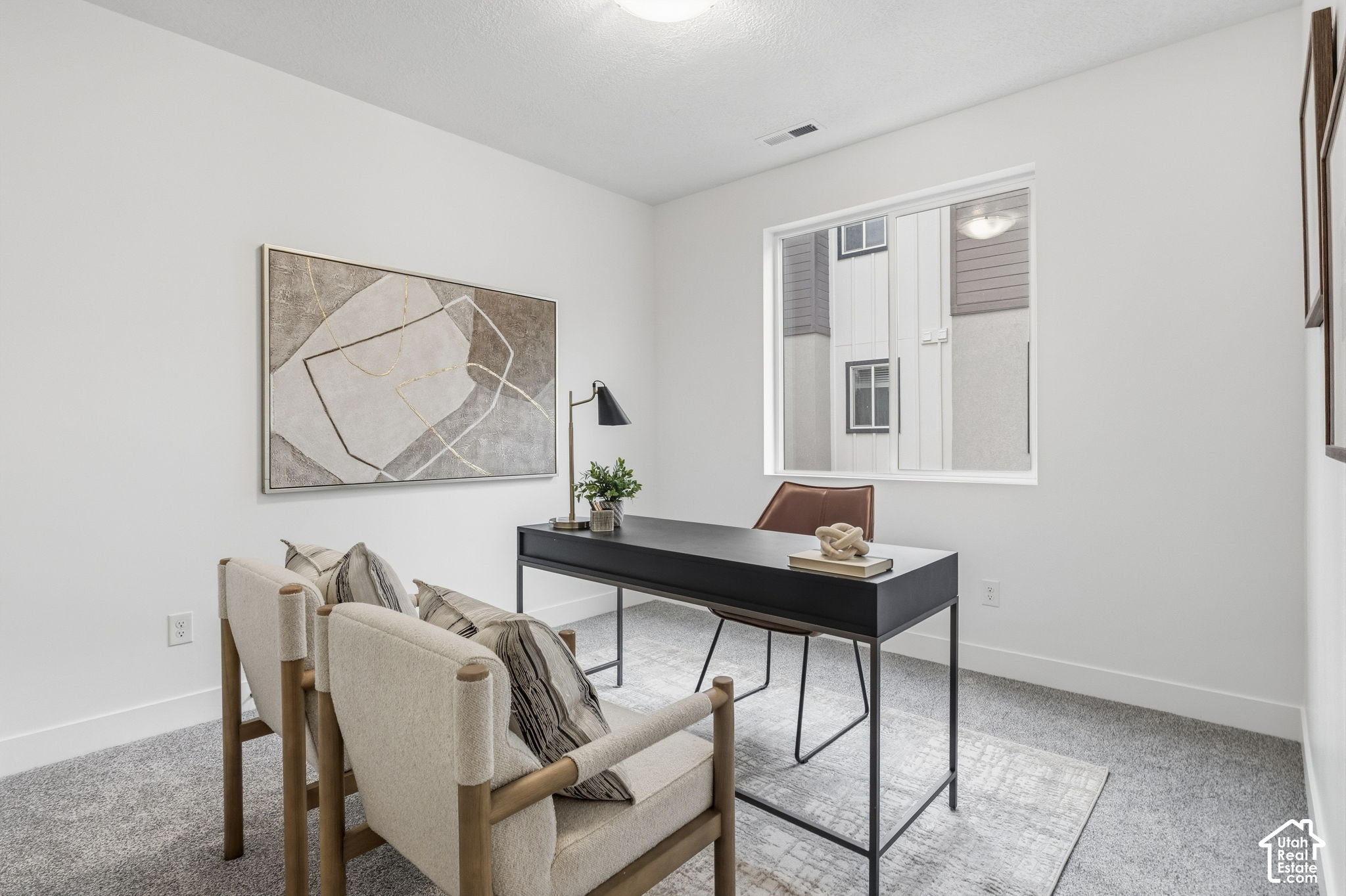 Staged home office with a black desk, upholstered guest chairs, and large abstract wall art.