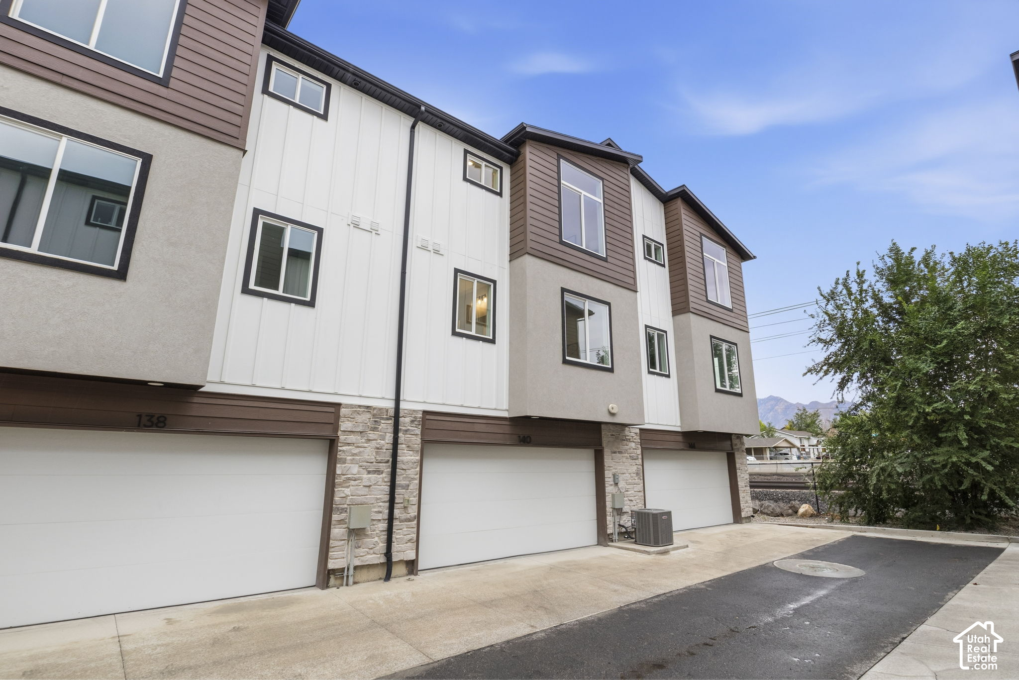 Modern townhouse exterior with white garage doors, stone accents, and distant mountains.