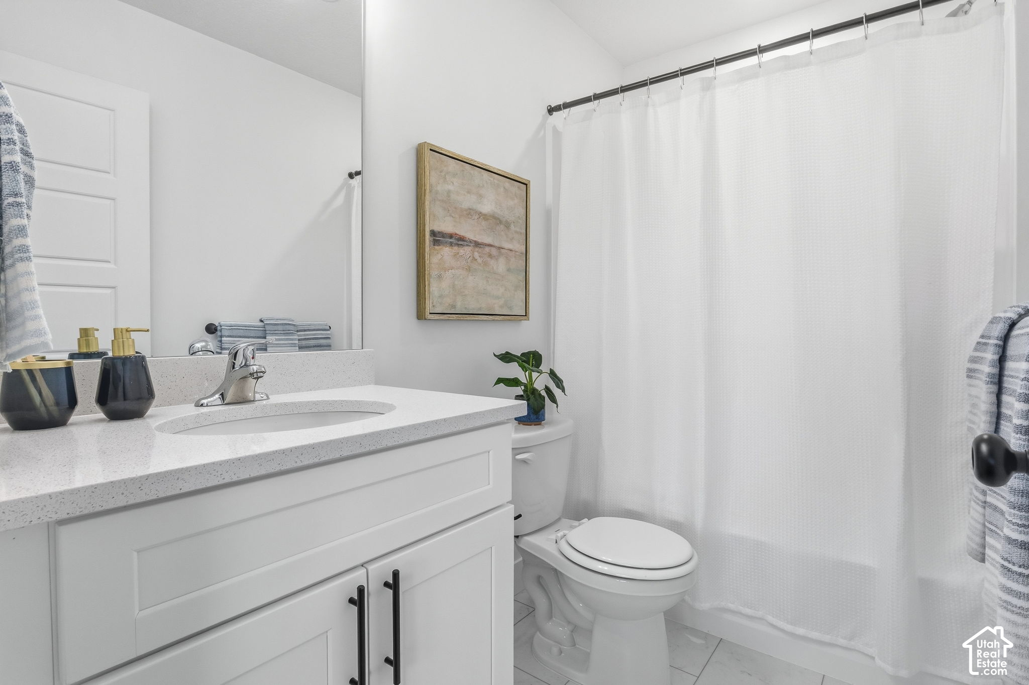 Bright bathroom with a white vanity, speckled countertop, shower curtain, and framed abstract art.