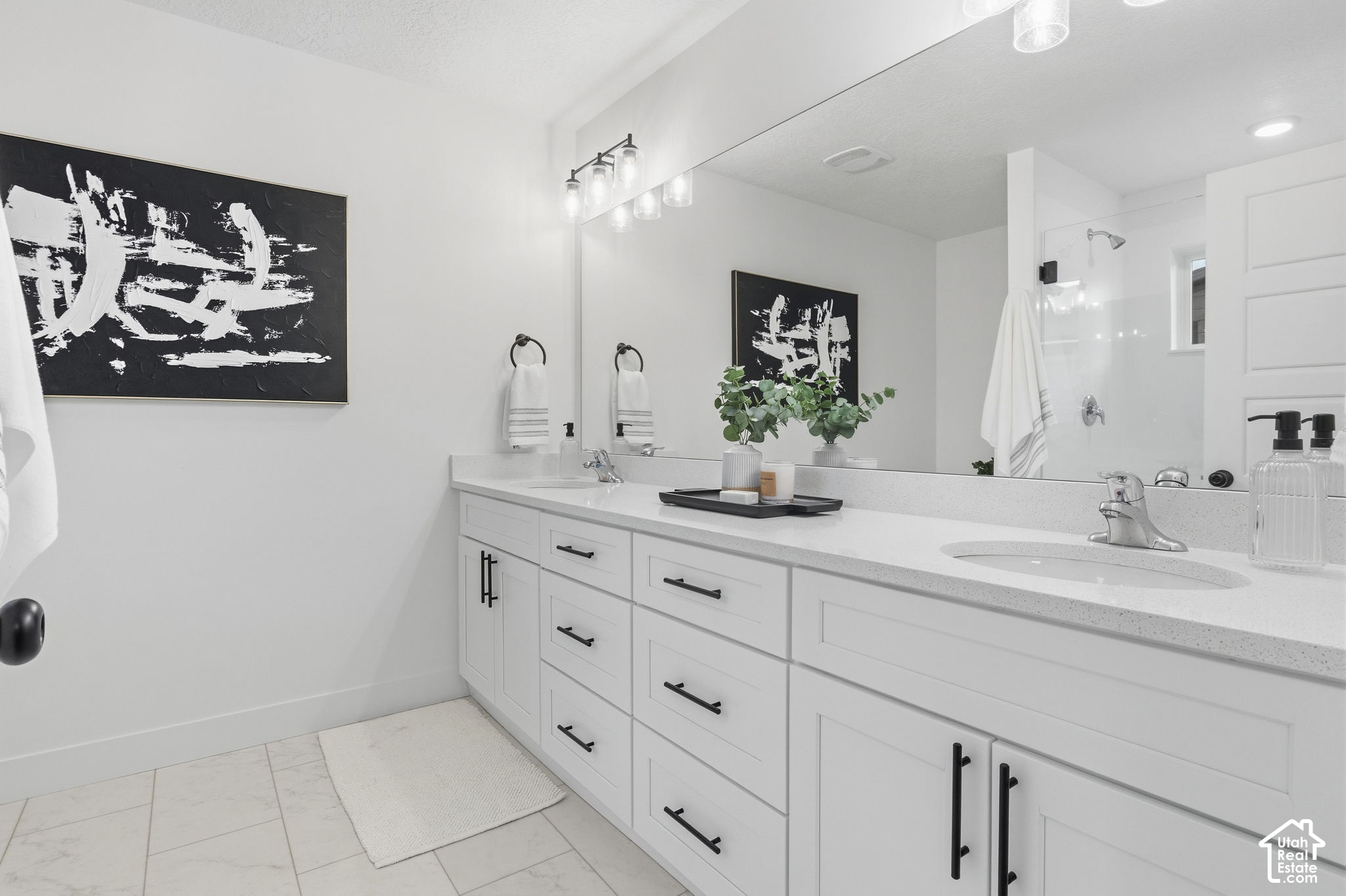 Bathroom with a long white double vanity, large mirror, and glass-enclosed shower.