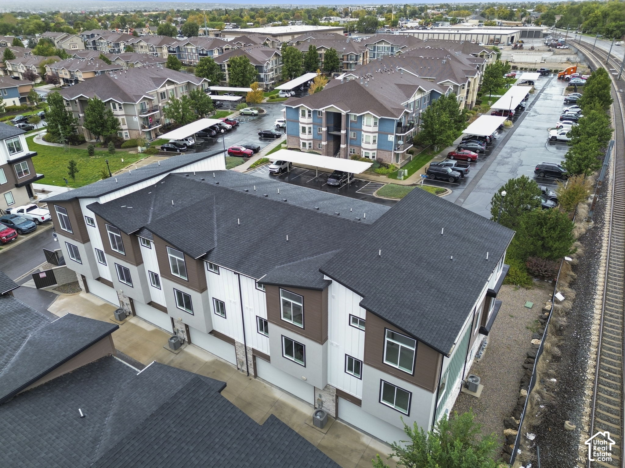 Aerial view of townhomes beside an apartment complex, parking lots, and railroad tracks.