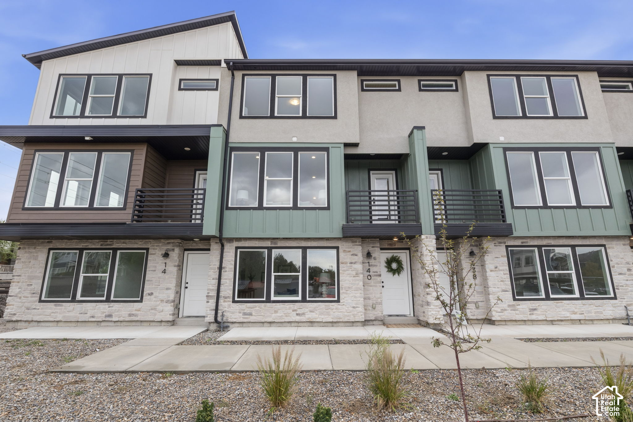 Townhouse exterior with white stone façades, muted green siding, and black-railed balconies.