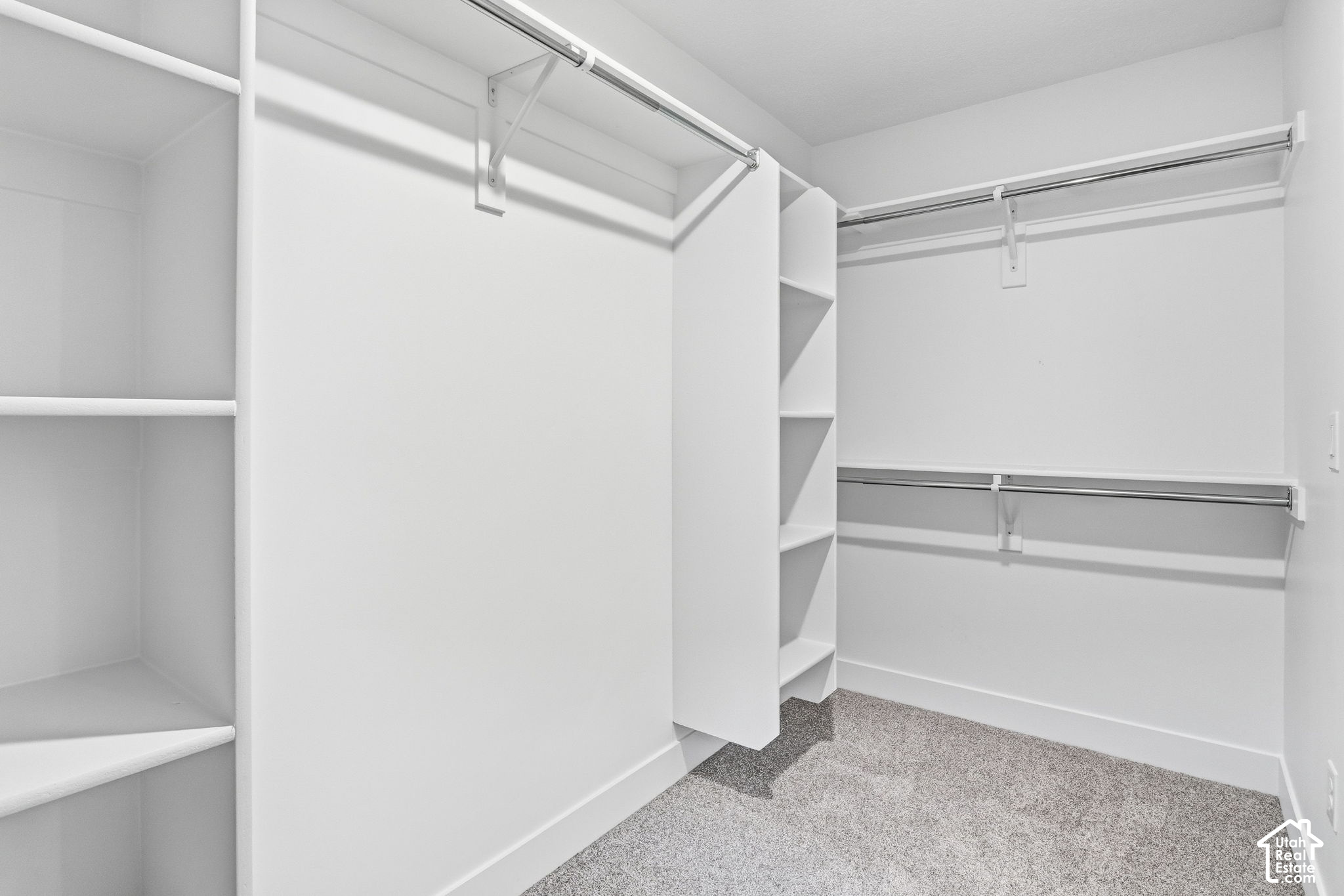 Empty walk-in closet with built-in shelves, clothes rods, and gray carpet.