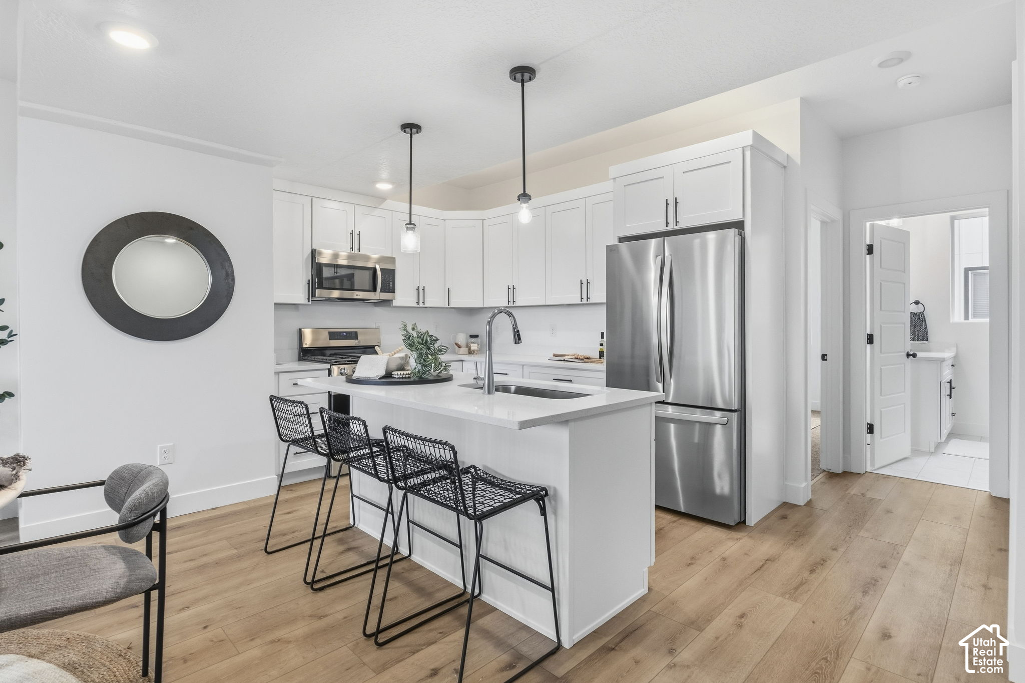 Bright white kitchen with a large island, stainless steel appliances, and black wire bar stools.