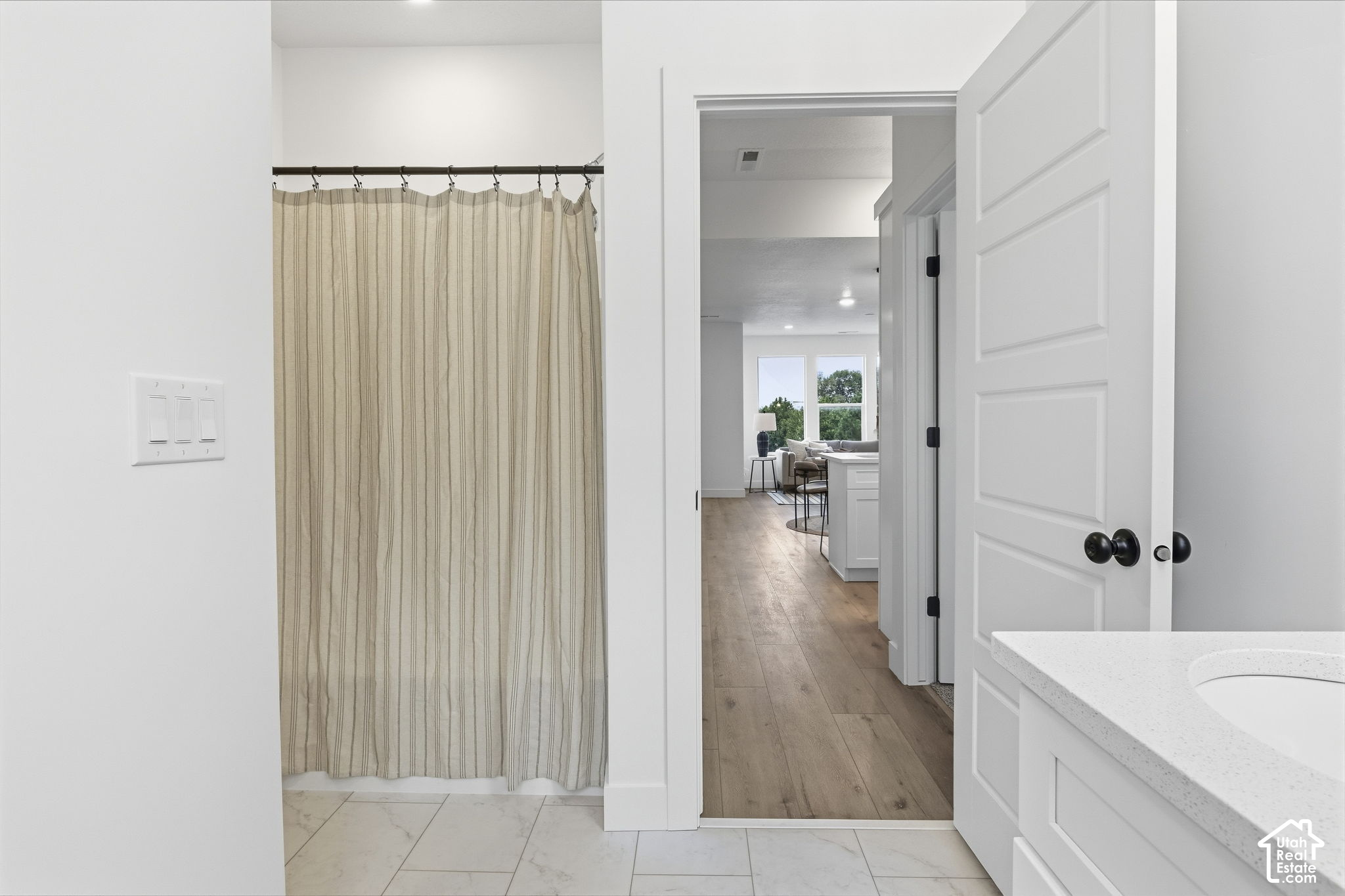 Bathroom with a striped shower curtain and white vanity, opening onto a wood-floored hallway.