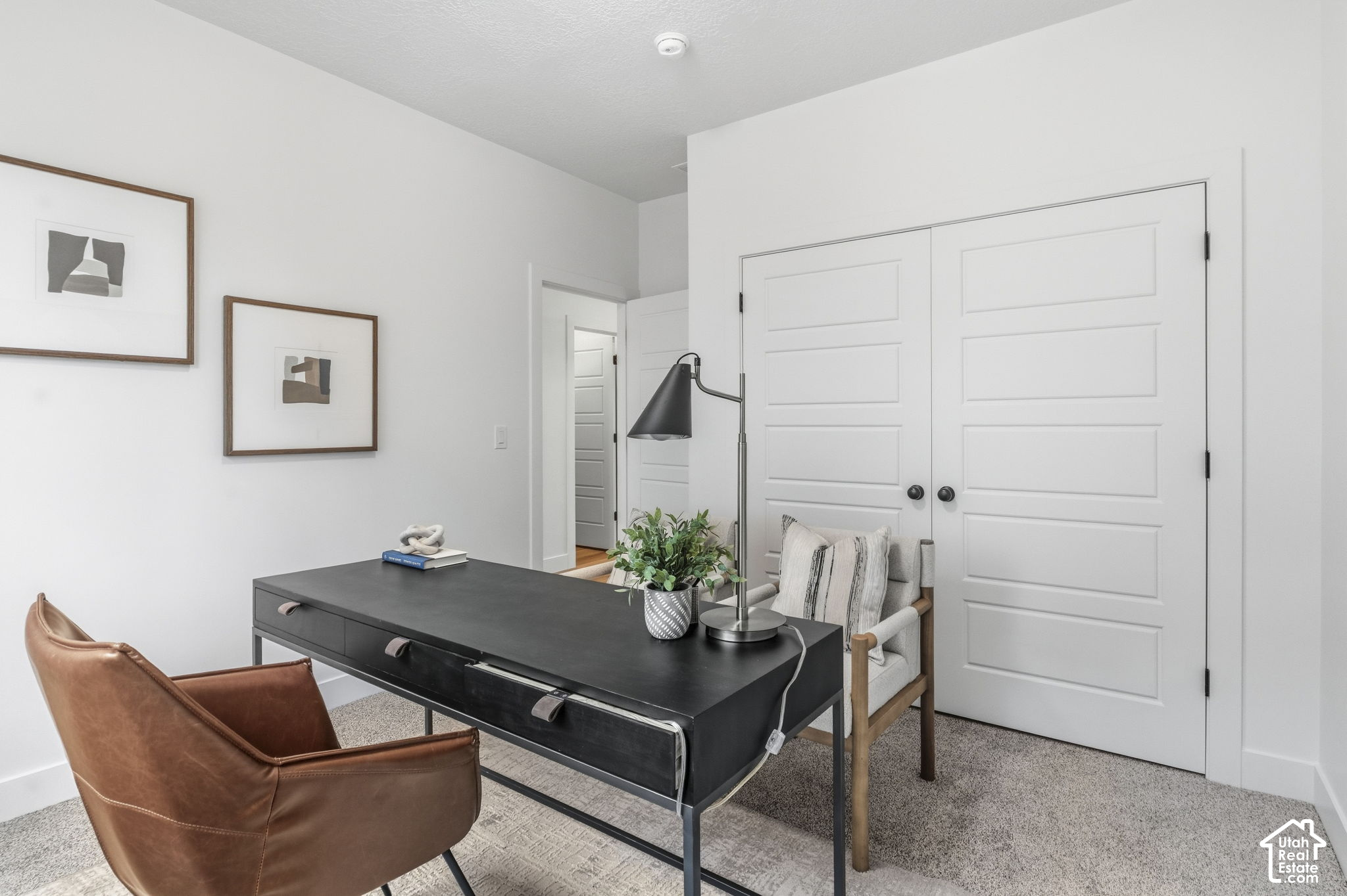 Staged home office with a black desk, brown leather chair, and white double doors.