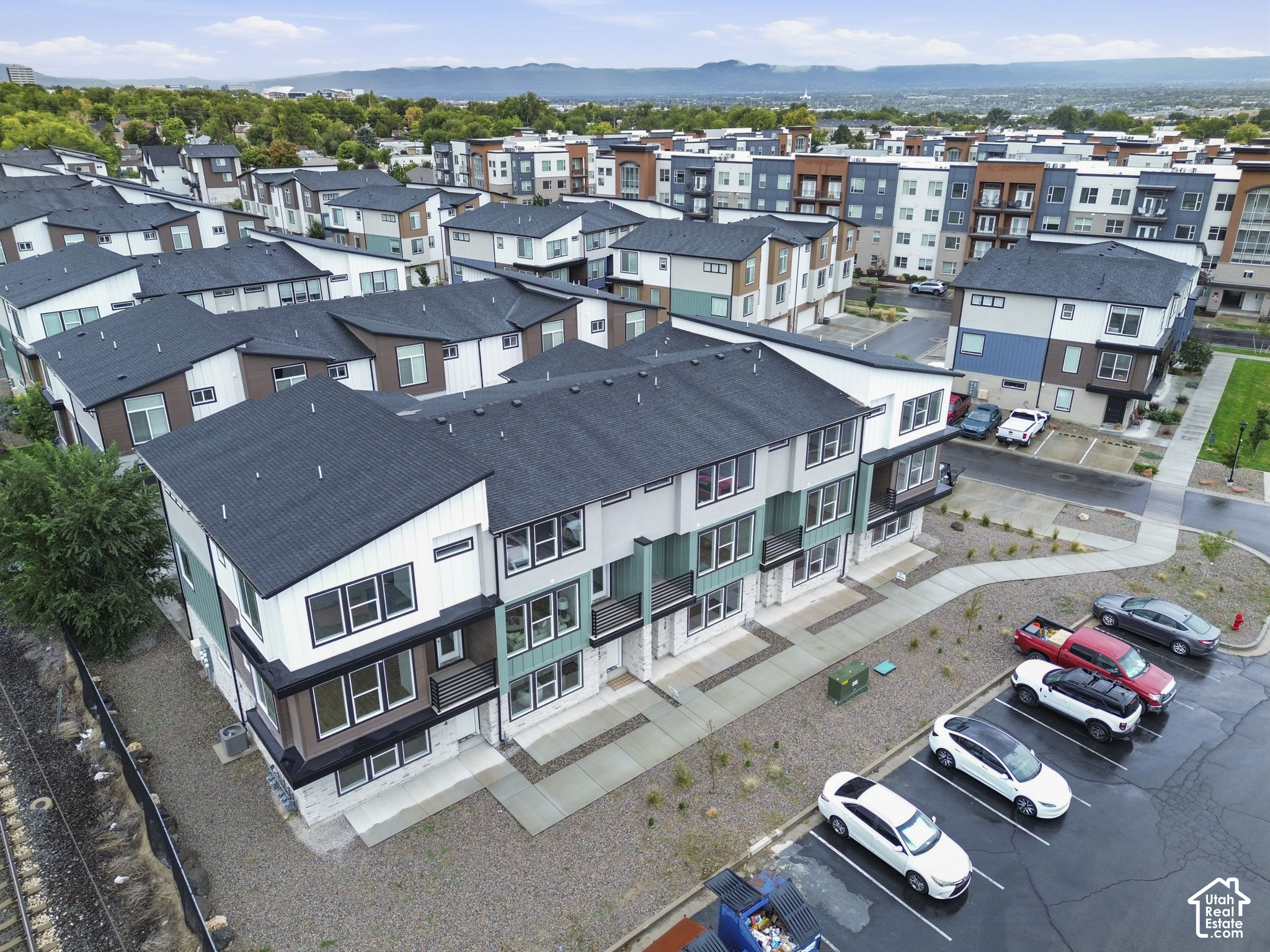 Aerial view of attached homes with dark roofs, parking, and mountains in the distance.