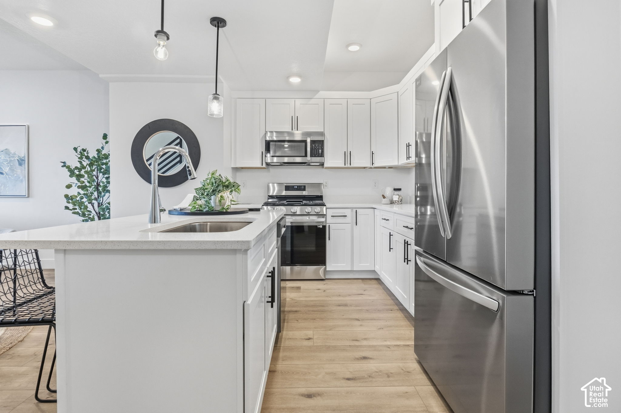 Modern white kitchen with a large island, stainless steel appliances, and light wood floors.