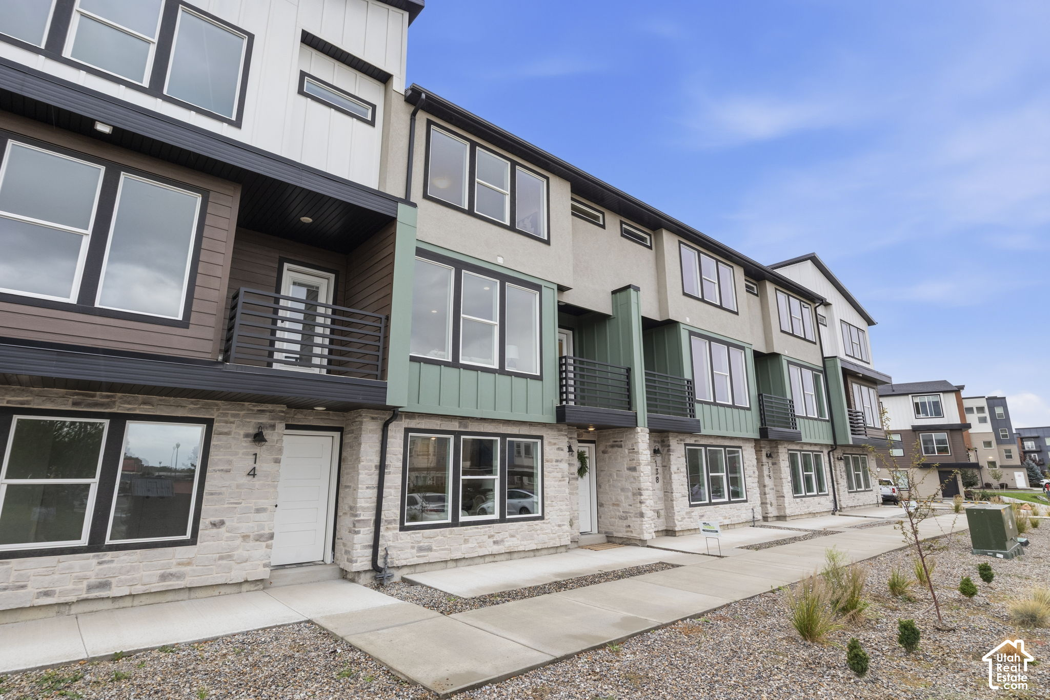 Modern townhome row with stone façades, green balcony panels, and landscaped gravel frontage.