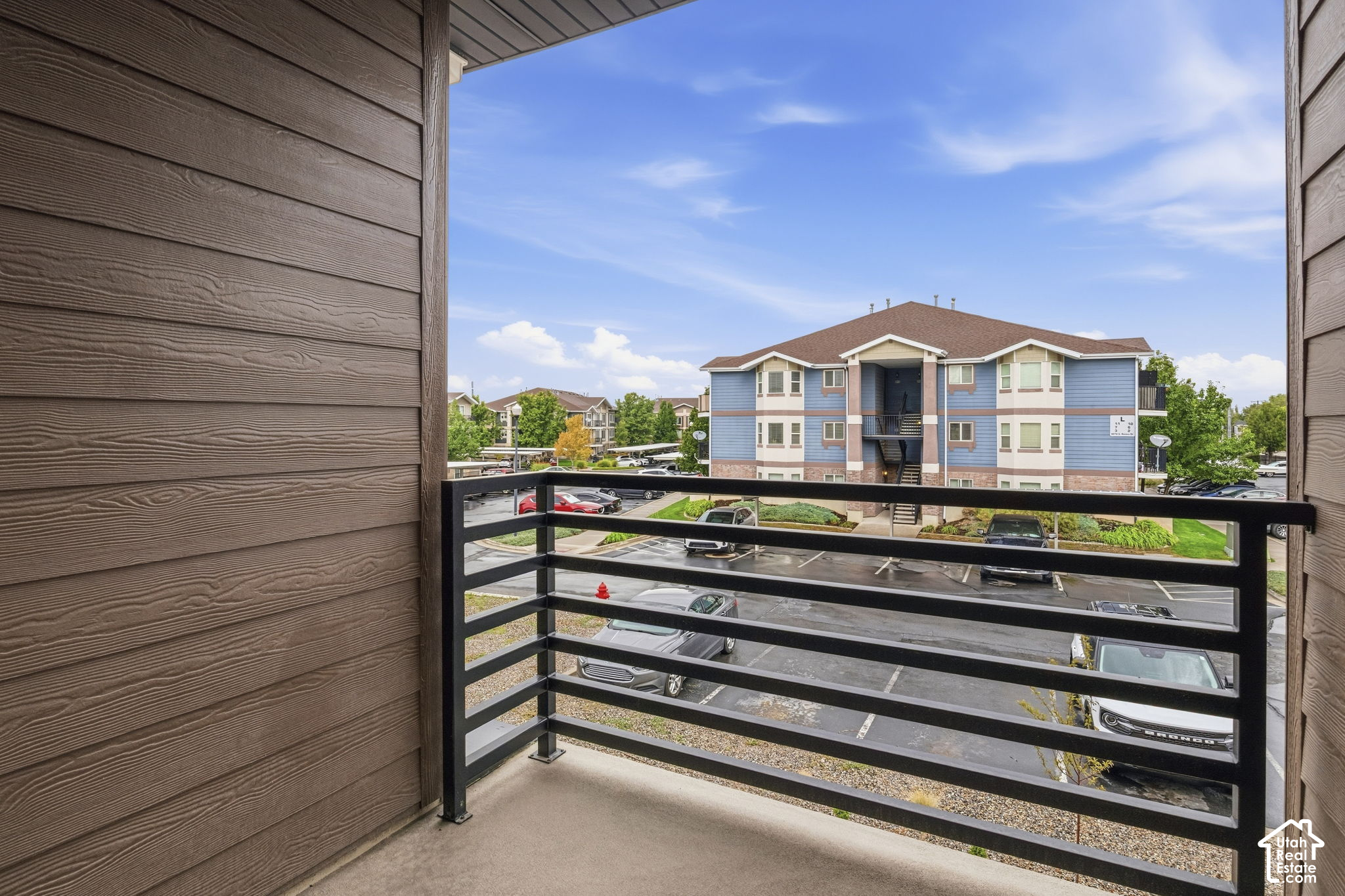 Covered balcony overlooking a parking lot and blue-and-cream apartment building.