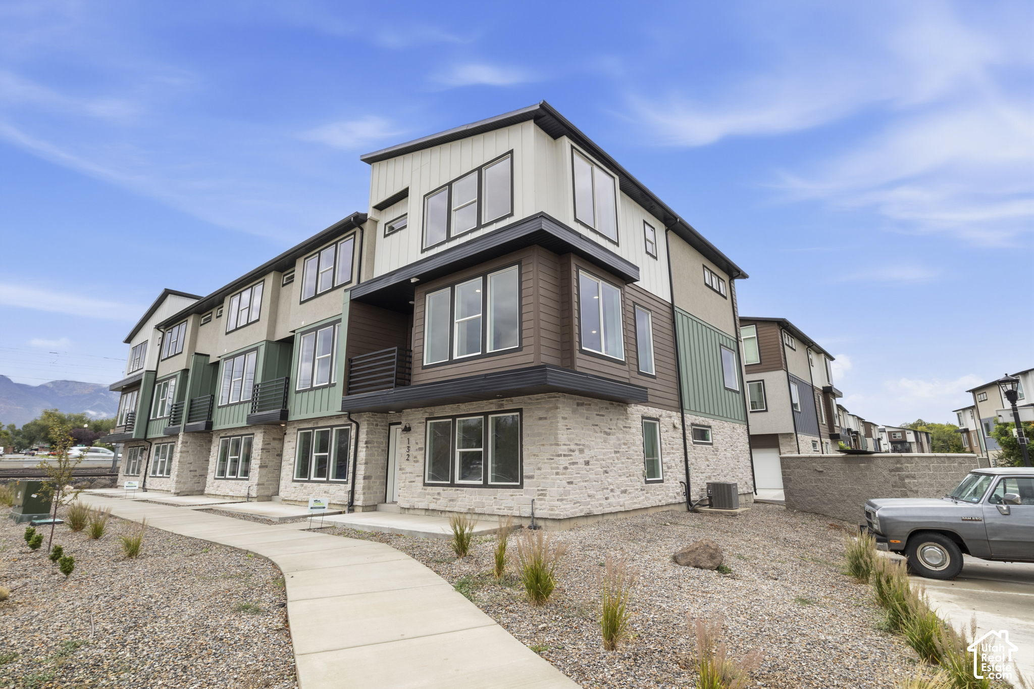 Modern multi-unit building with stone cladding, green and brown siding, and a curved front walkway.