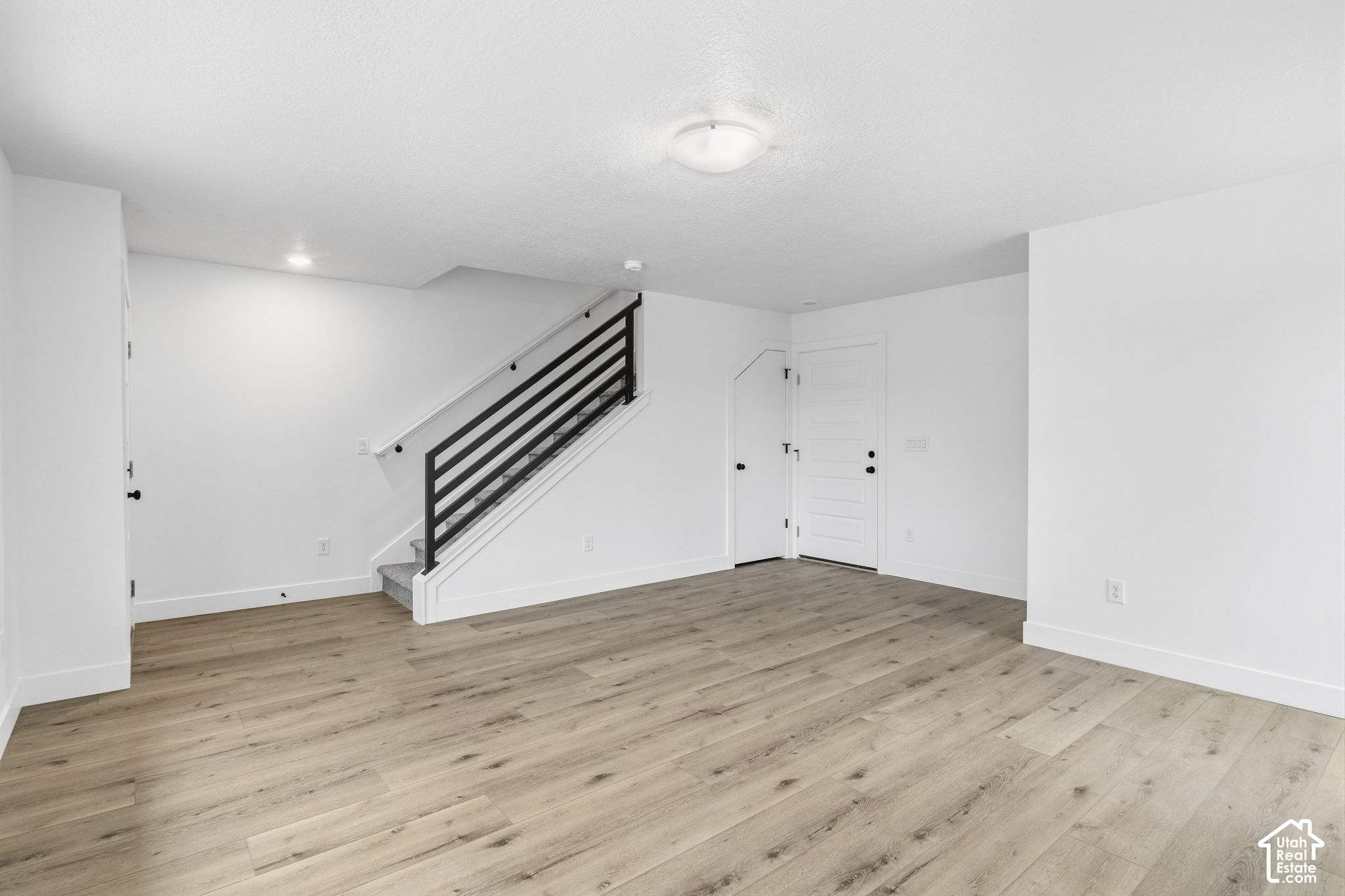 Empty interior with light wood-look flooring and a staircase with black horizontal railing.