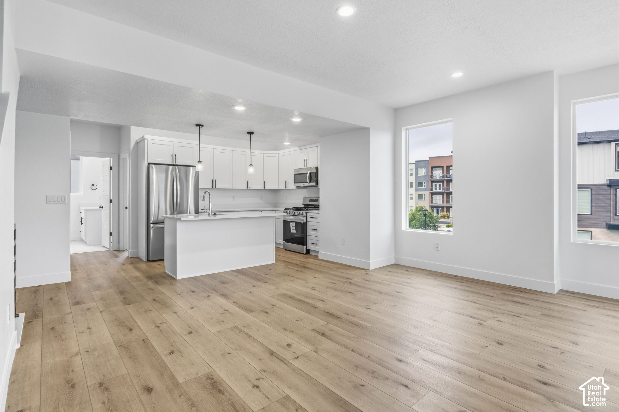Open-plan kitchen and living area with a white island, stainless appliances, and light wood floors.