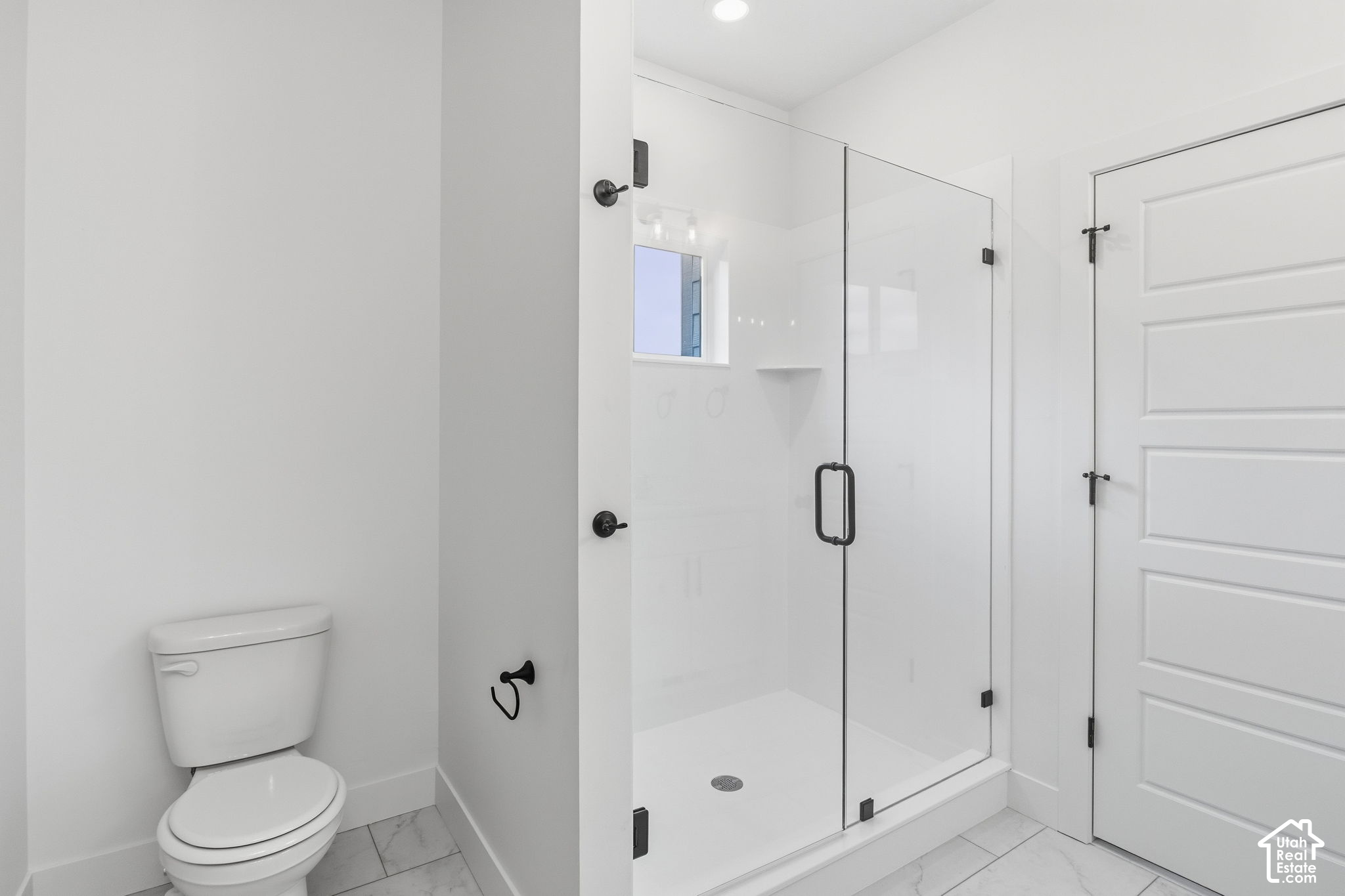 Bathroom with a glass-enclosed walk-in shower, black fixtures, and marble-look floor tile.
