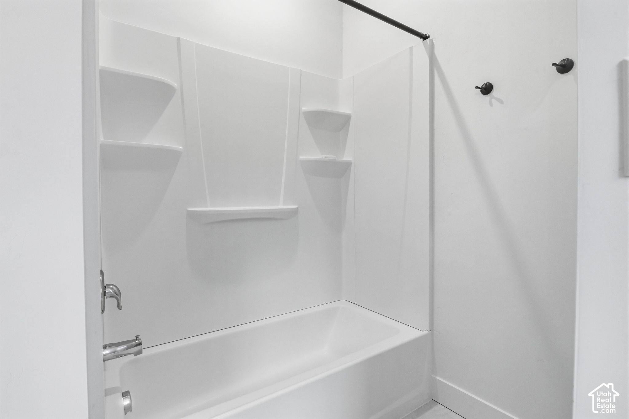 White bathtub and shower with molded shelves and dark fixtures.