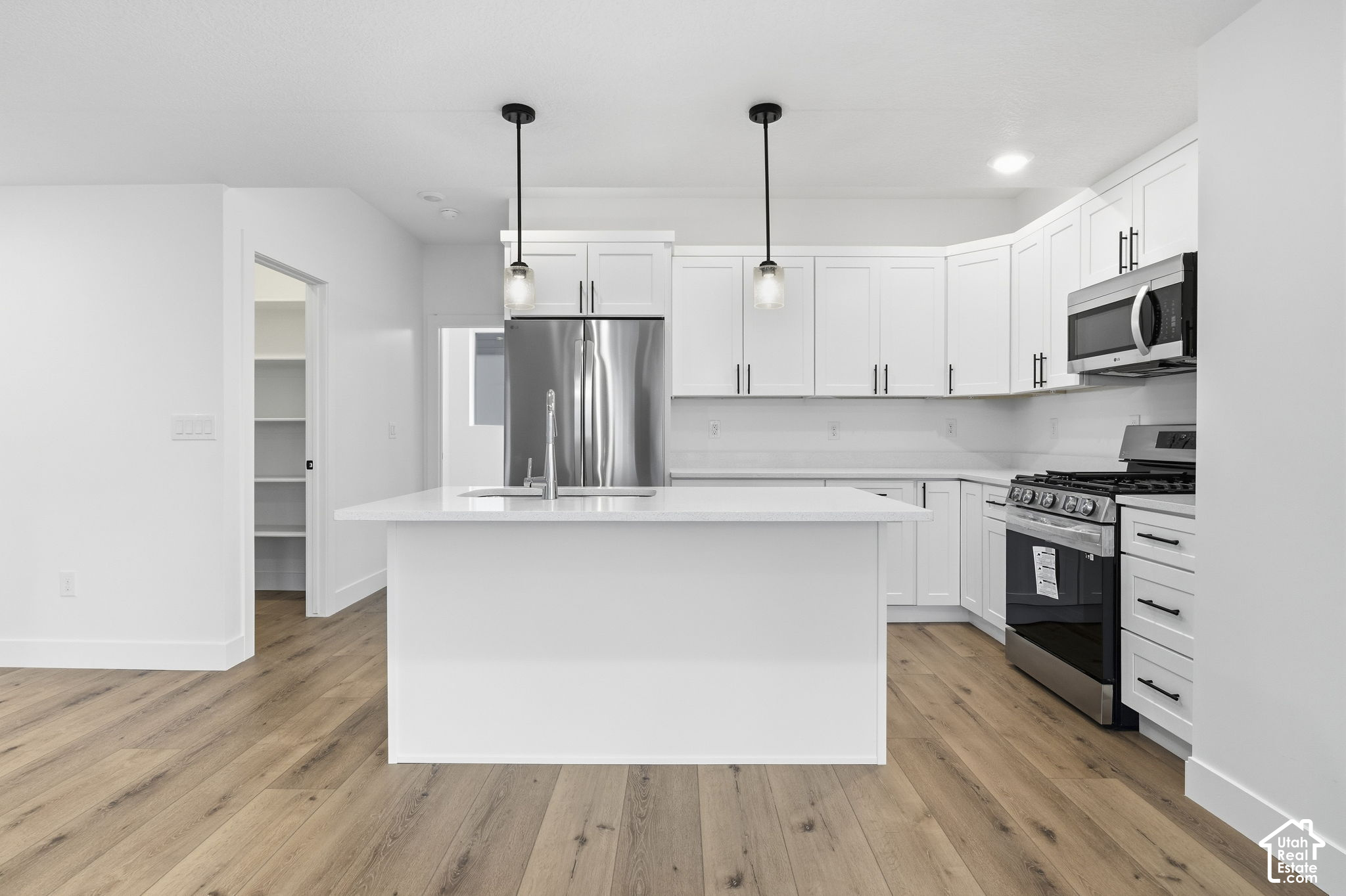 Bright kitchen with a large island, white cabinetry, stainless steel appliances, and wood-look flooring.