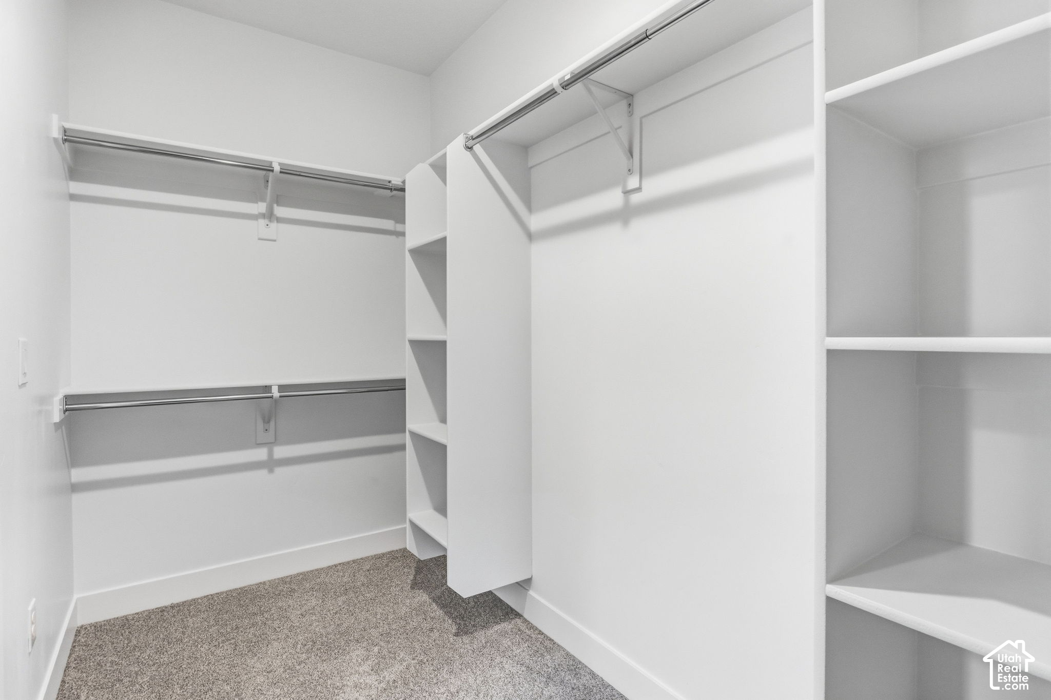 Walk-in closet with built-in shelving, hanging rods, and gray carpet.