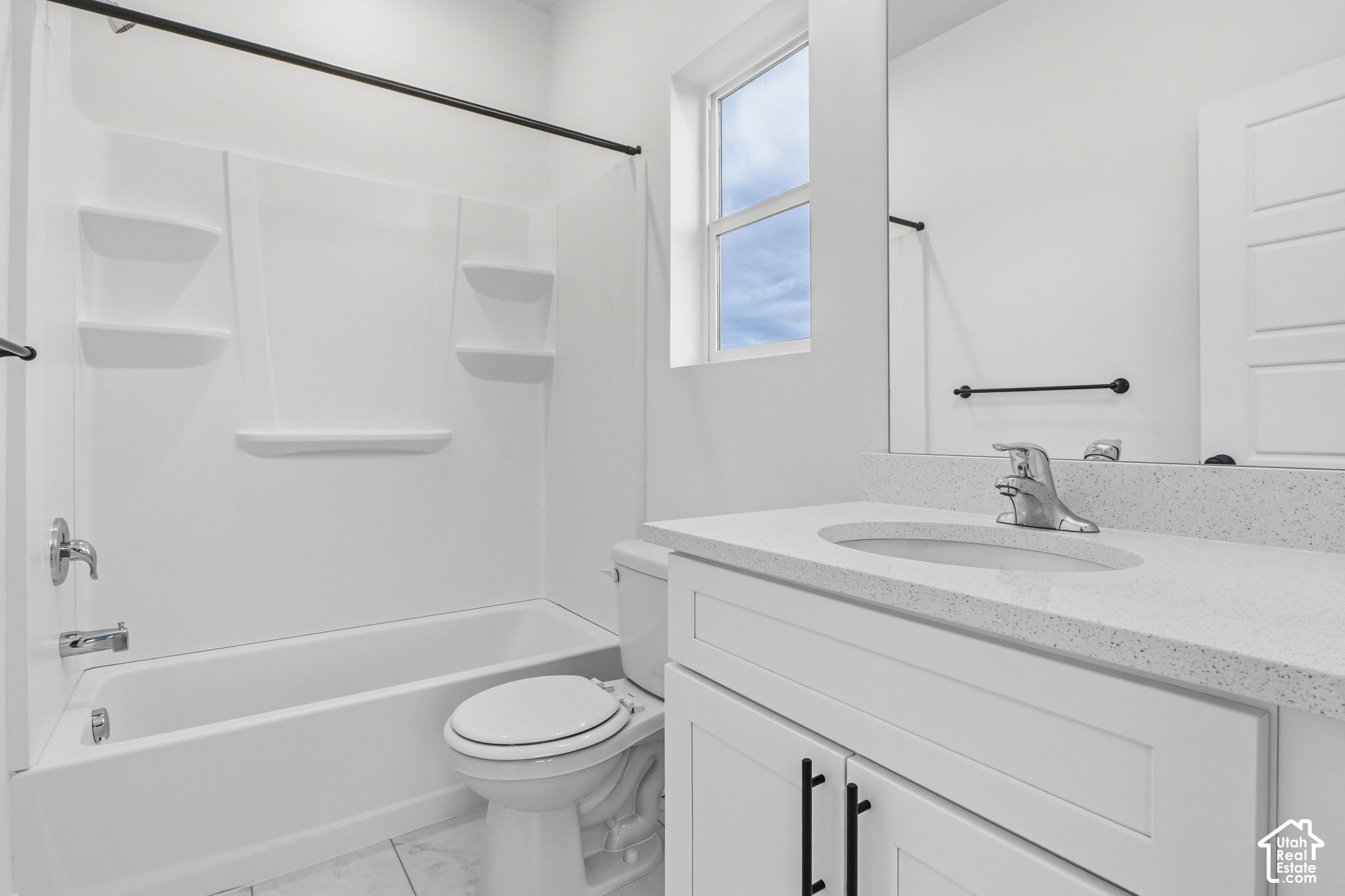 White bathroom with a bathtub, built-in shower shelves, toilet, and speckled vanity countertop.