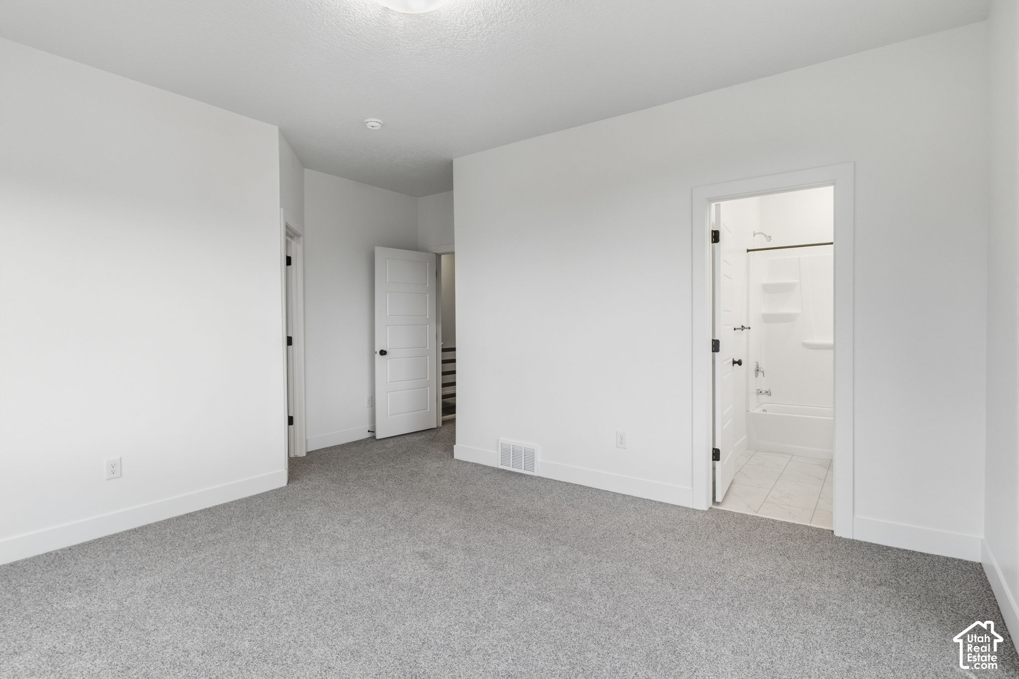 Empty bedroom with gray carpet and an open doorway to a bathroom with a tub and shower.