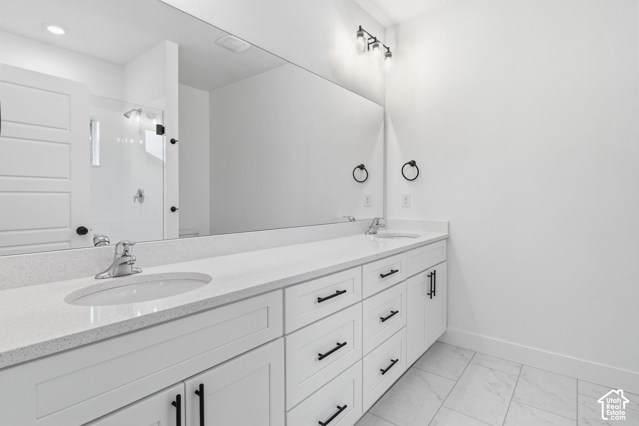 Bright bathroom with a long white vanity, speckled countertop, black pulls, large mirror, and glass shower.
