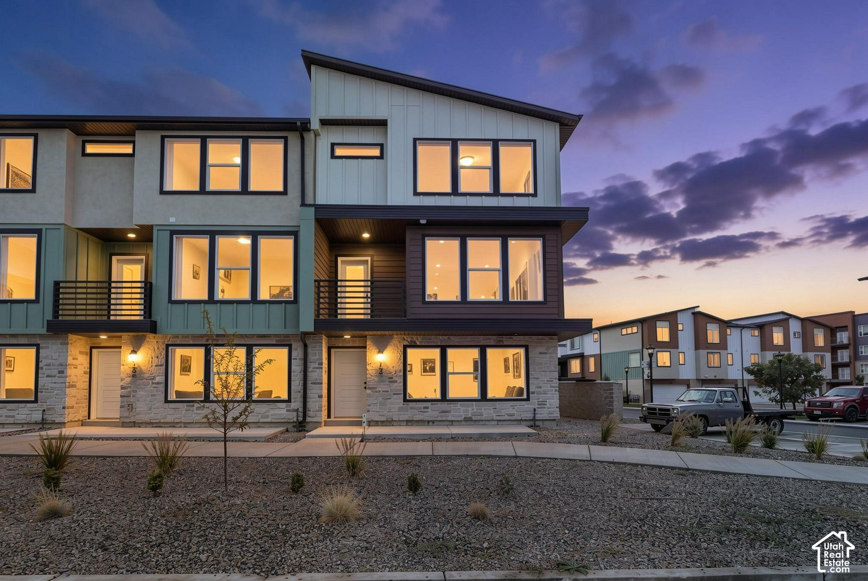 Modern multi-story townhome with stone facade and glowing windows at dusk.