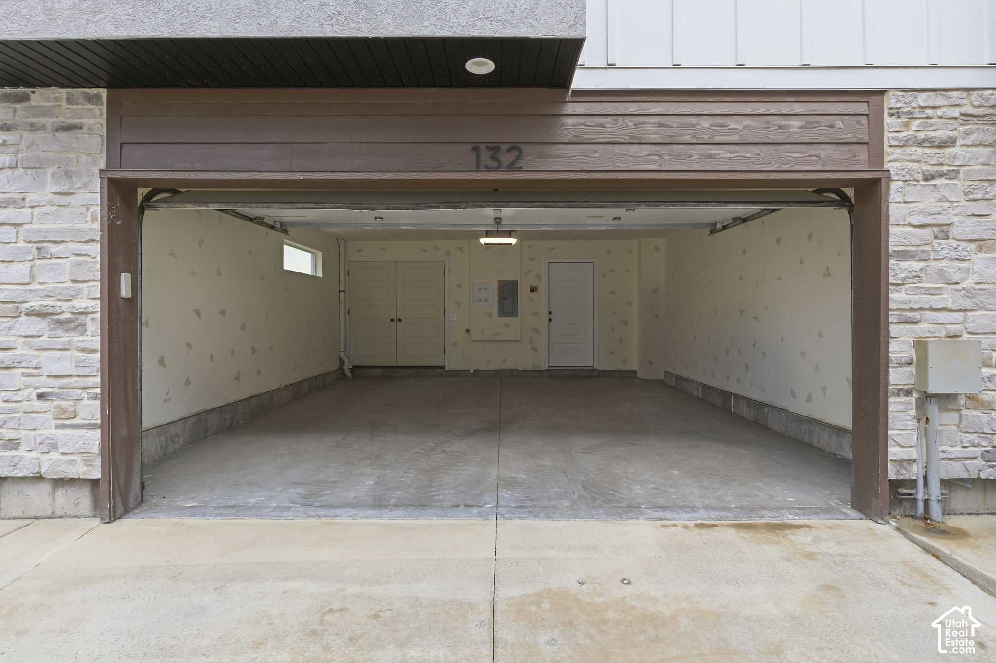 Open, empty two-car garage with a concrete floor and house number 132 above the entrance.