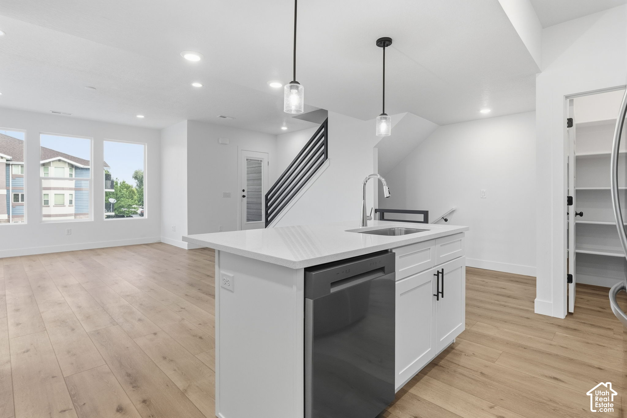 Open-plan kitchen with a large white island, dark dishwasher, light wood floors, and black metal staircase.