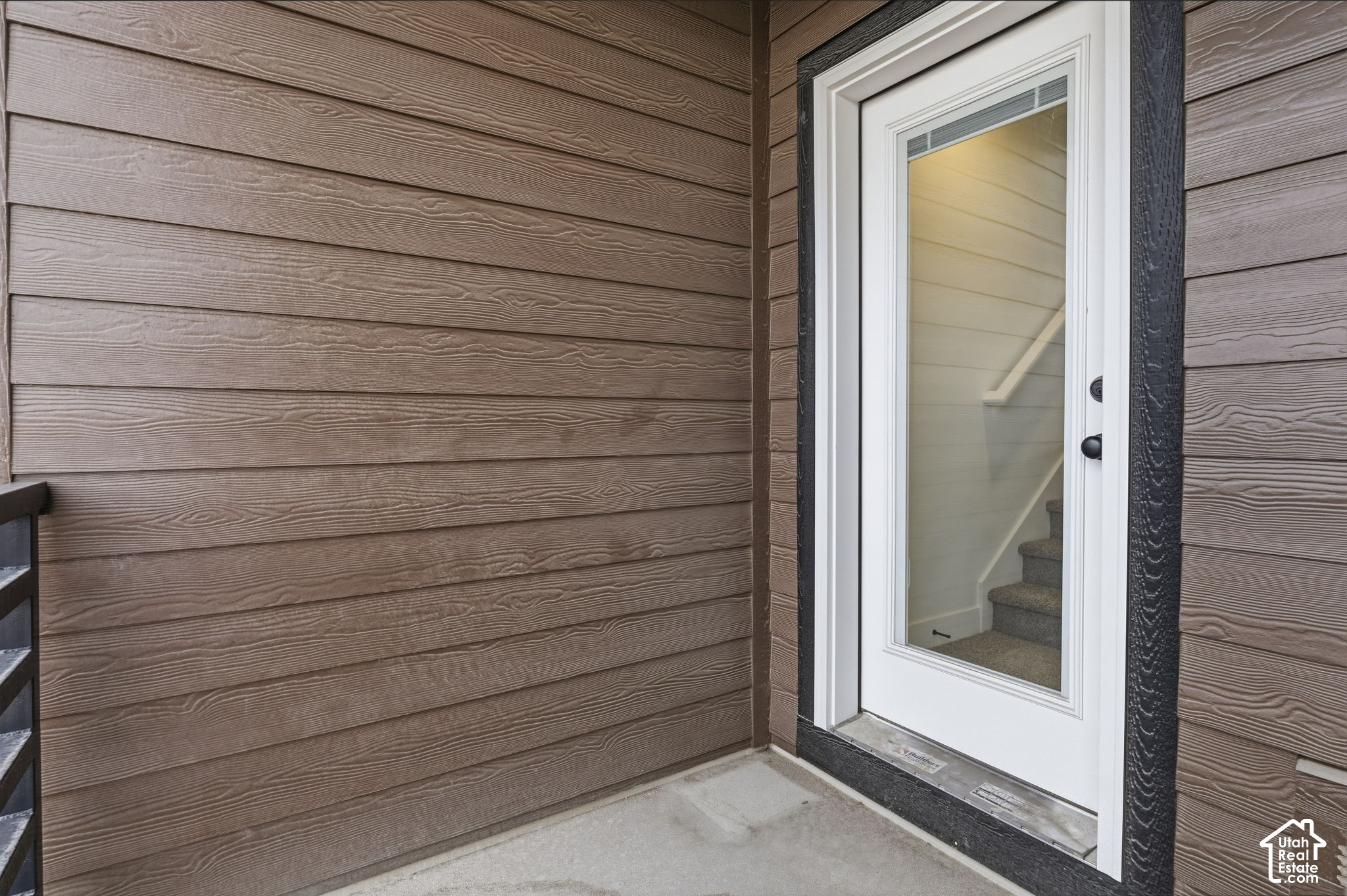 White glass-paneled entry door in brown siding, with an interior staircase visible through the glass.