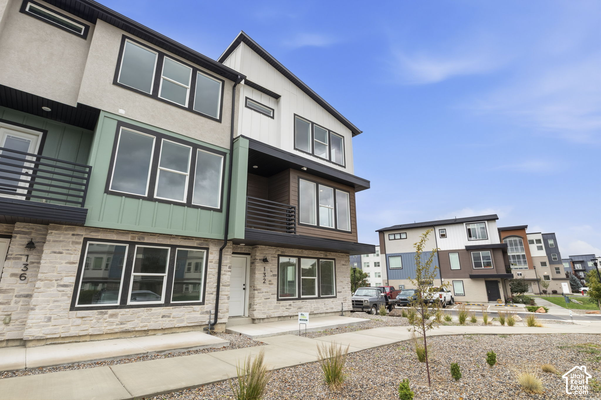 Modern multistory townhouse with stone ground floor, green-and-white siding, and covered balconies.