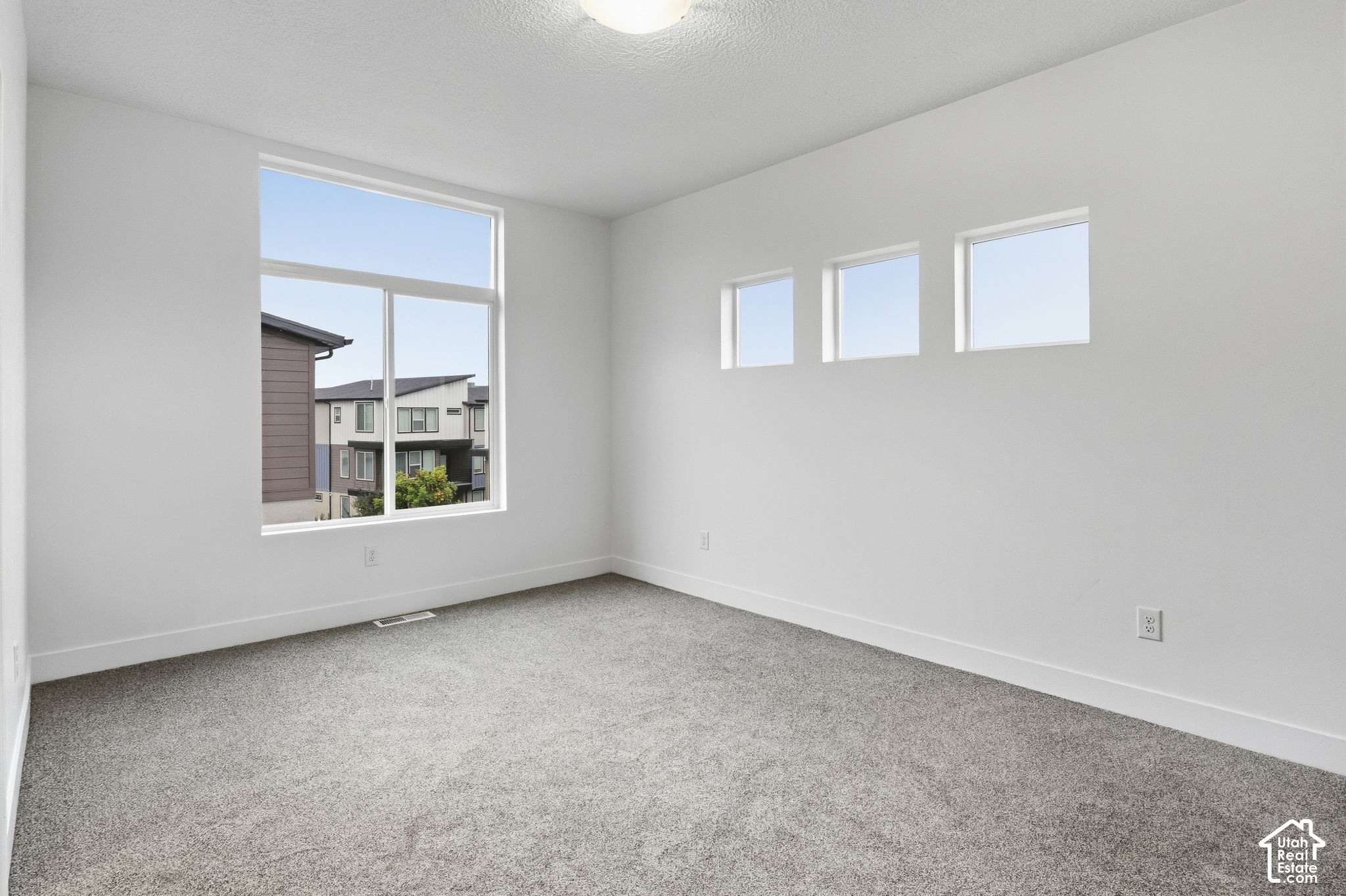 Empty carpeted bedroom with a large window and three smaller high-set windows.