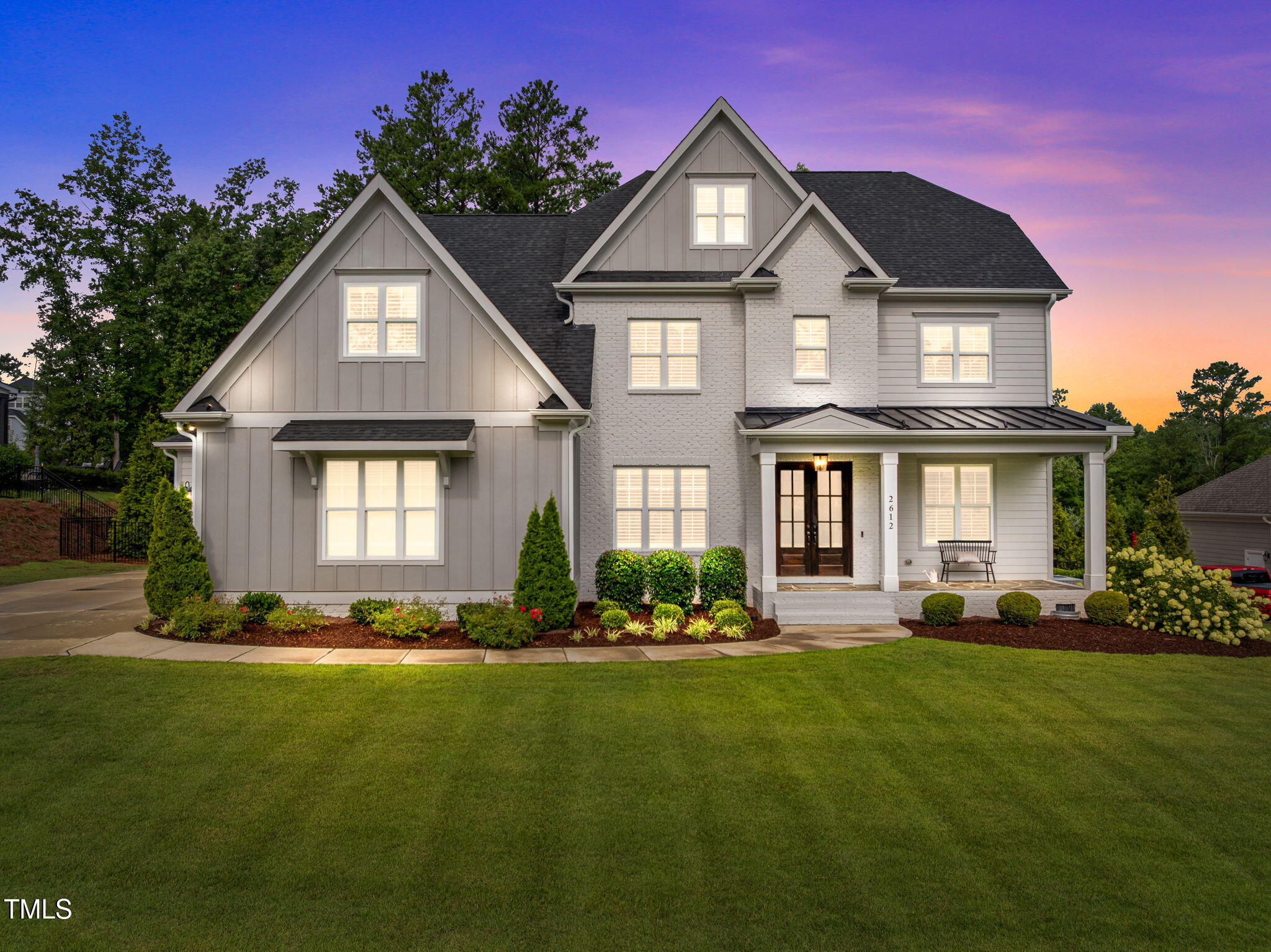 Two-story gray and white house with multiple gables and a covered porch at dusk.