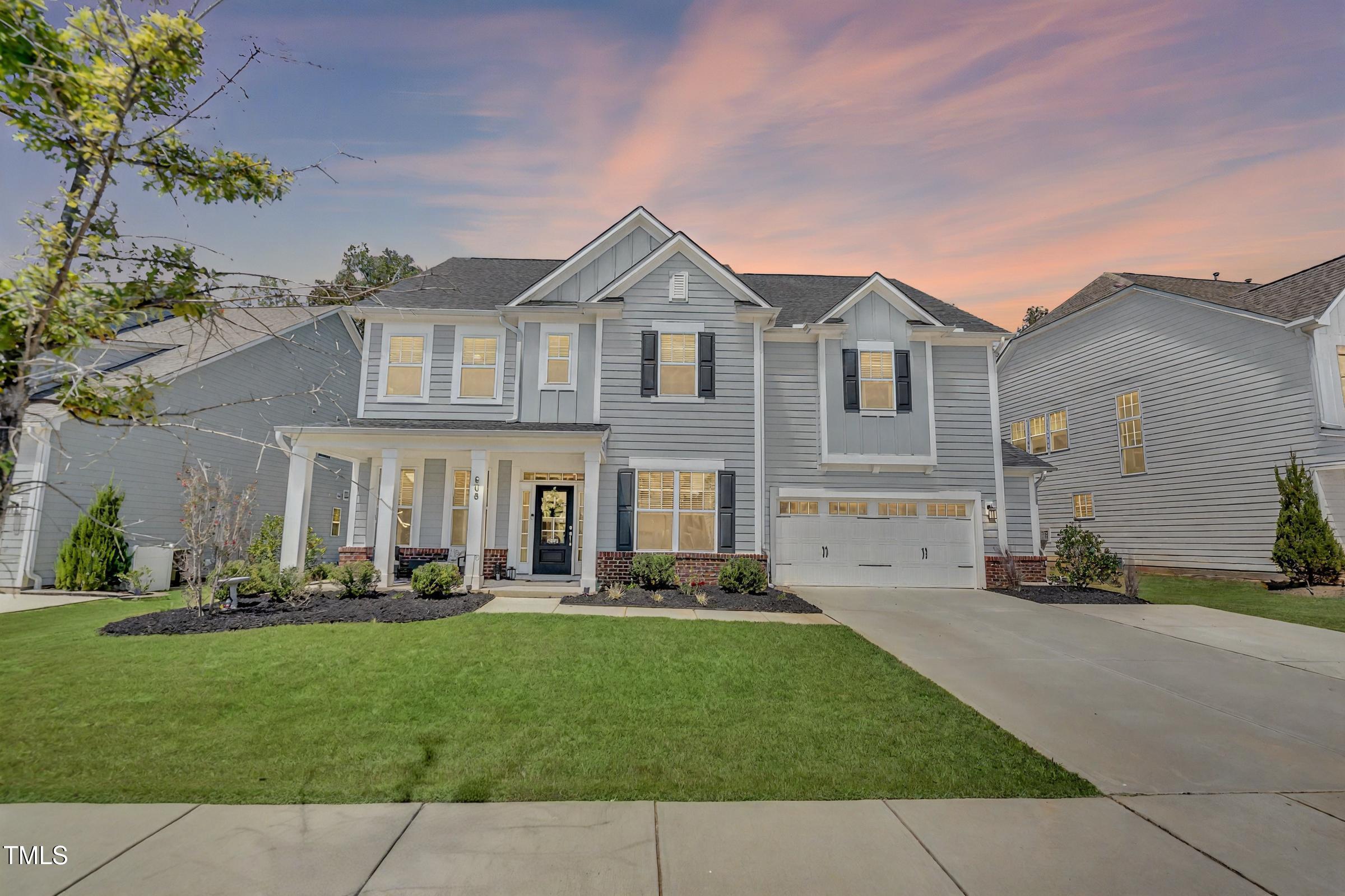 Two-story gray home with a covered porch, attached garage, and landscaped front lawn at dusk.