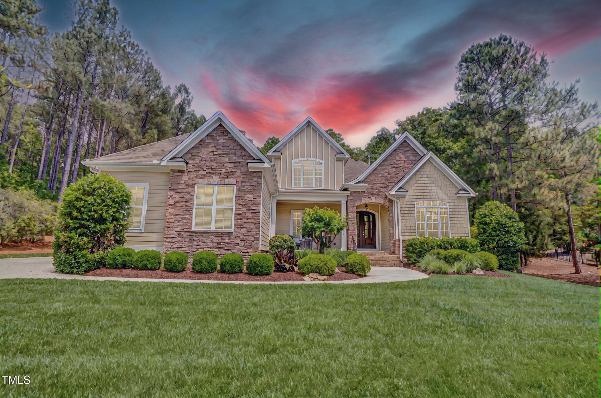 Two-story stone-and-siding home with a landscaped lawn and pine trees beneath a pink dusk sky.